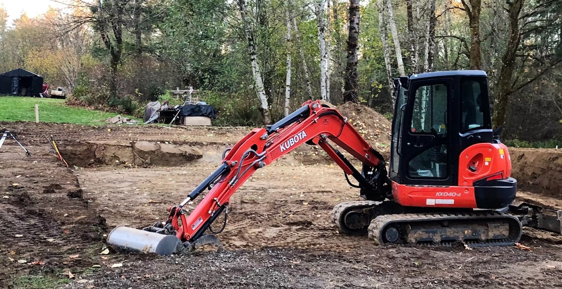 Orange mini excavator clearing dirt in a wooded construction site
