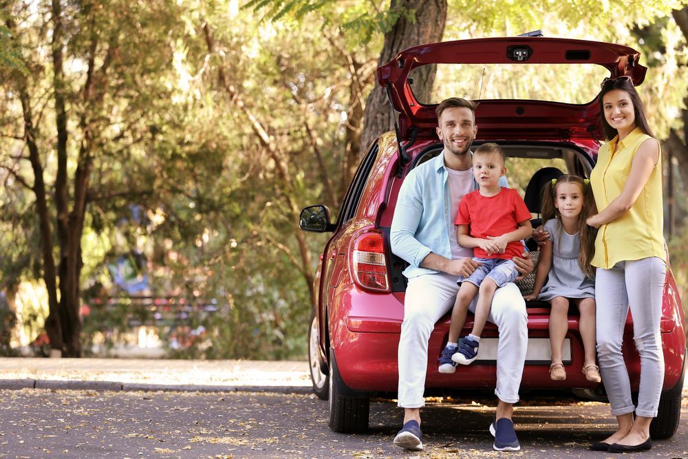 A family is sitting in the back of a red car.