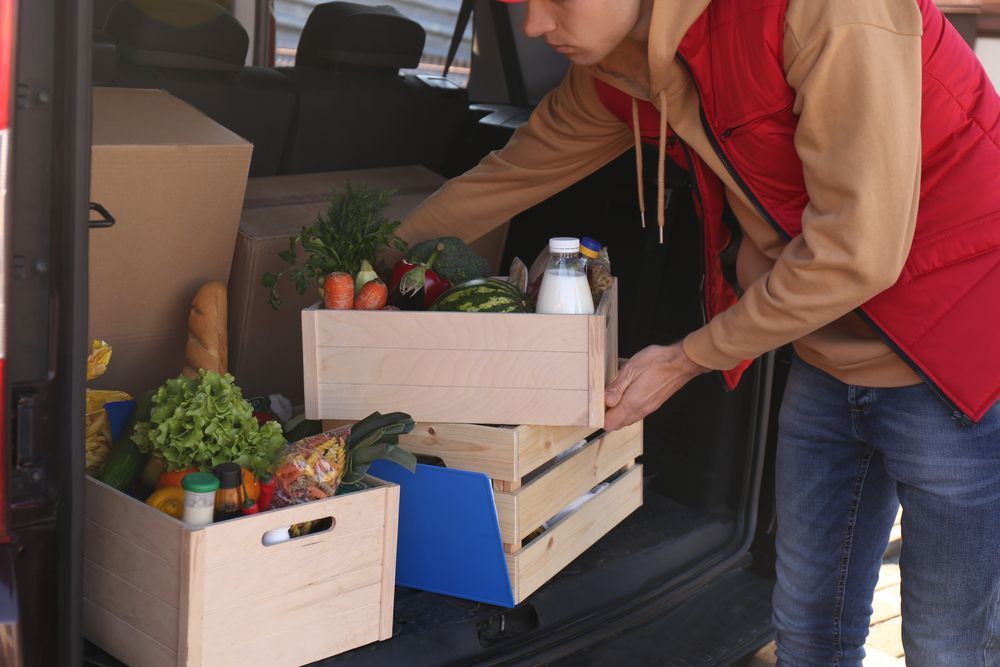 A man is loading crates of food into the back of a van.