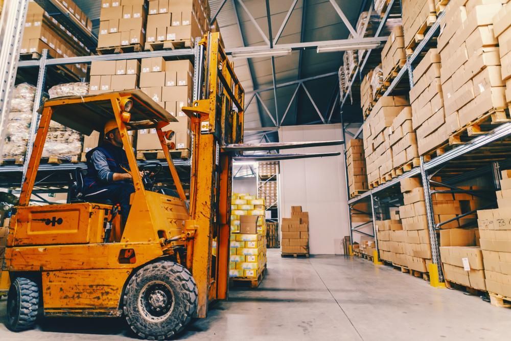 Man is Driving a Forklift in a Warehouse Filled With Boxes — Bundaberg Forklift Repairs Maryborough, QLD