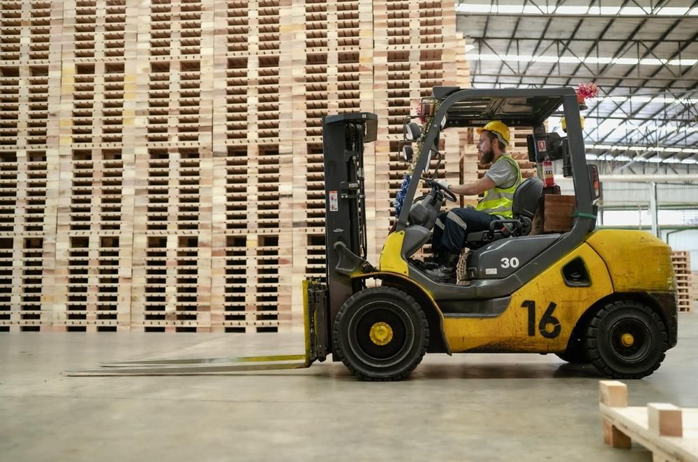 Man is Driving a Forklift in a Warehouse Filled With Wooden Pallets — Bundaberg Forklift Repairs Agnes Water, QLD 