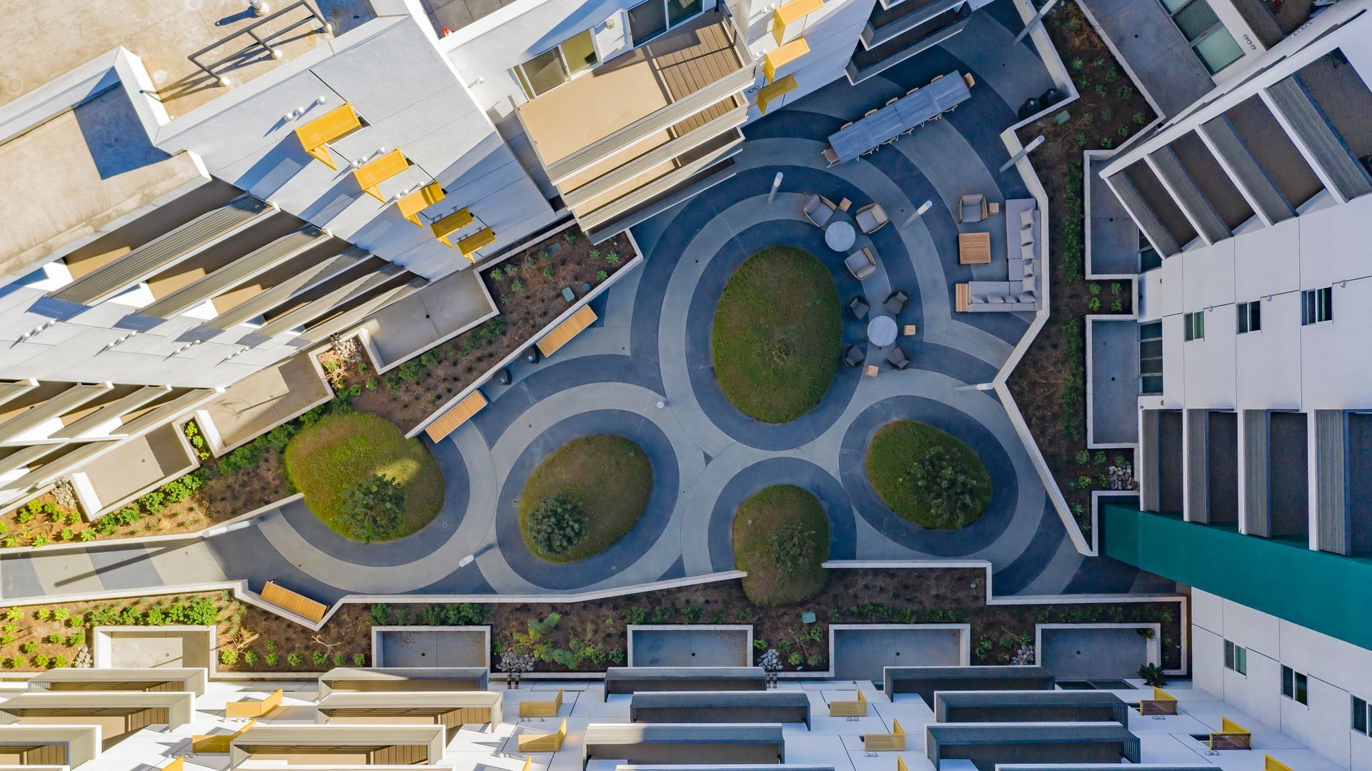 Aerial view of a modern apartment courtyard with circular paths, green lawns, and surrounding buildings