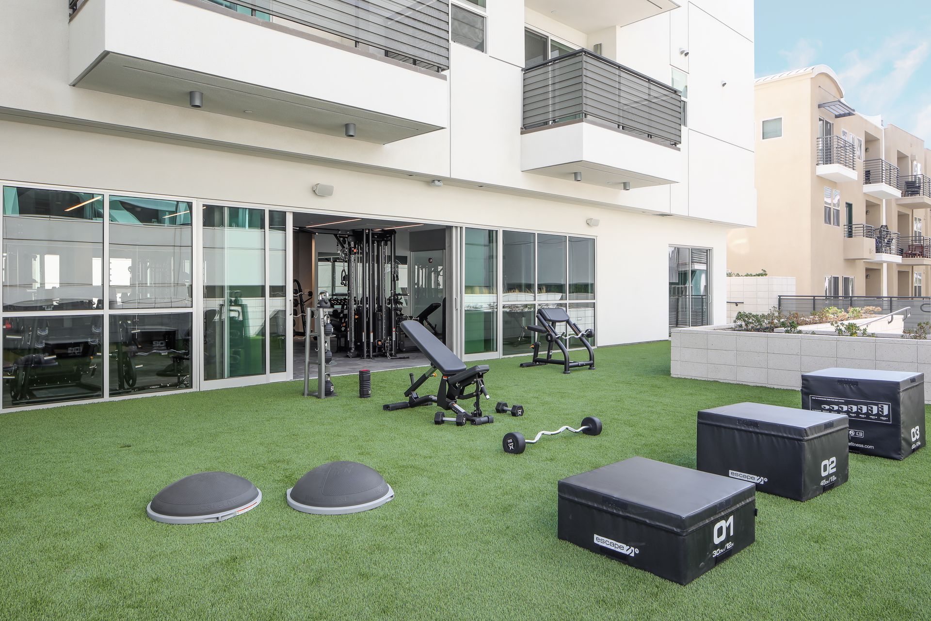 Outdoor gym equipment on a grass patio beside a modern apartment building