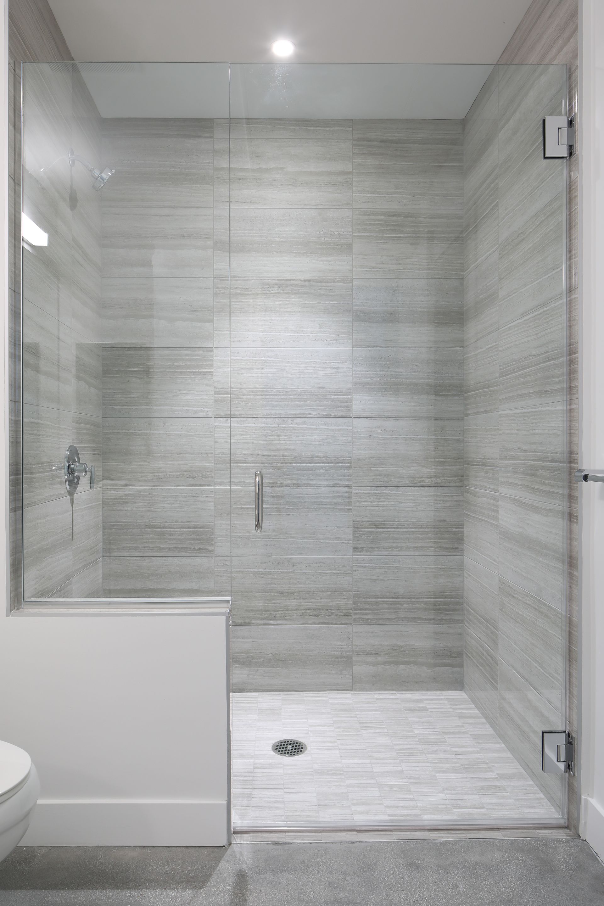 Modern tiled bathroom with glass shower enclosure and white tub edge