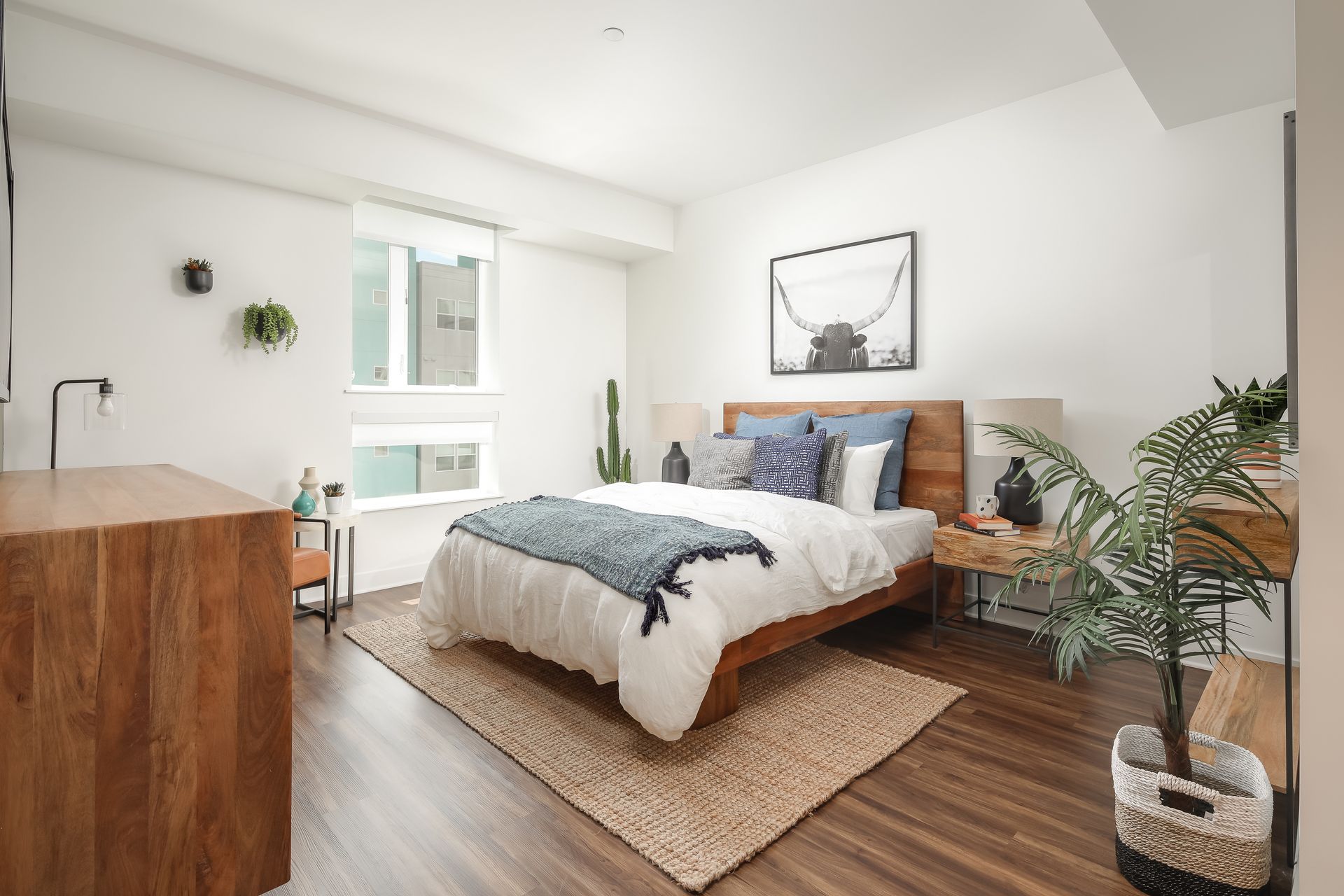 Bright minimalist bedroom with a bed, framed wall art, plants, and wood floors