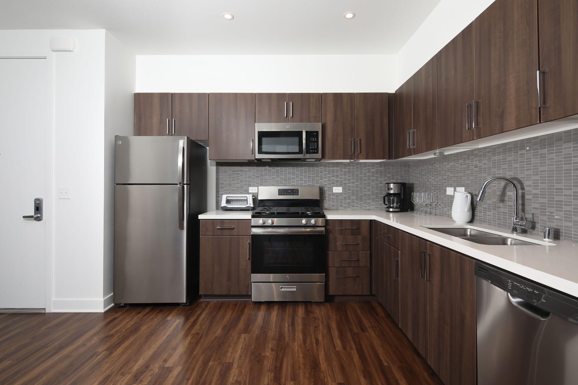 Modern kitchen with stainless steel appliances, dark wood cabinets, gray backsplash, and wood flooring