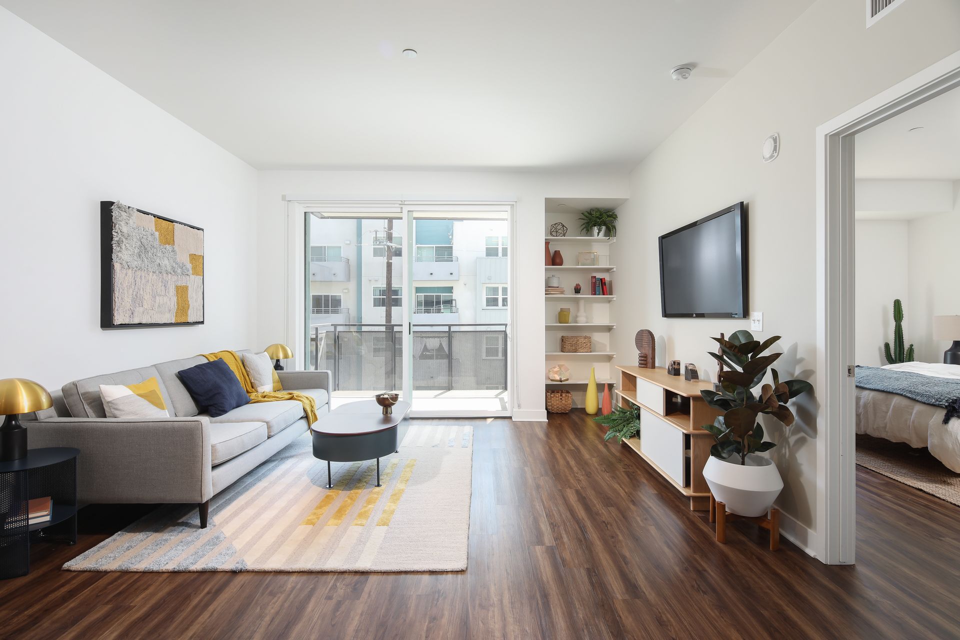 Bright modern living room with gray sofa, wall TV, wood floors, and balcony doors