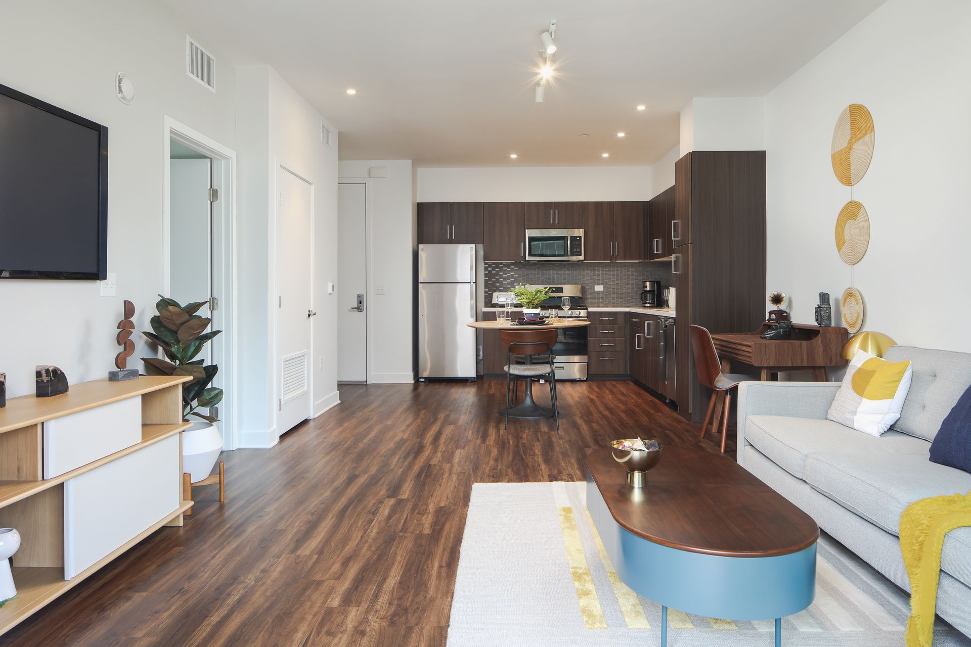 Modern open-plan living room with gray sofa, wood floors, and kitchen in the background