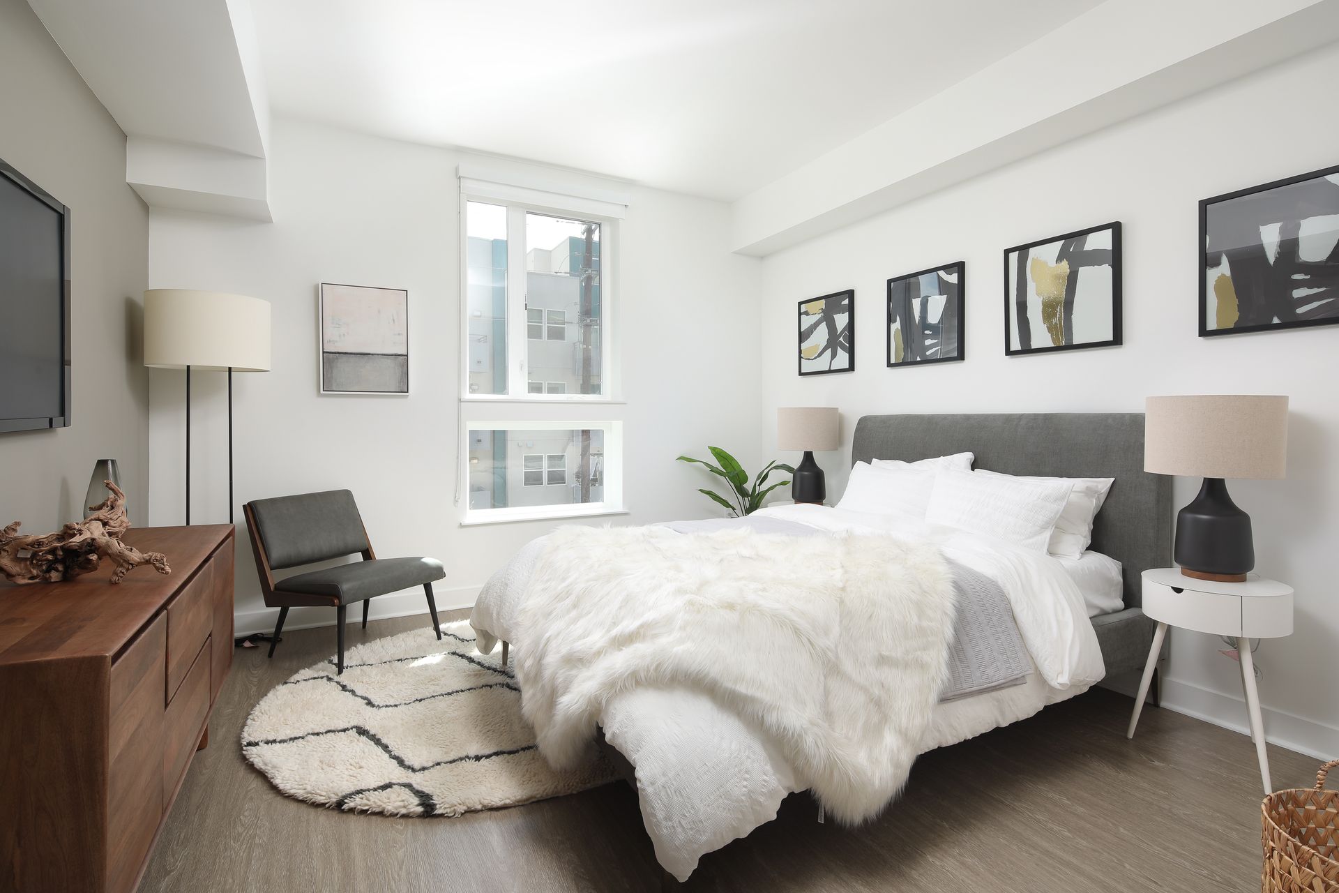Bright modern bedroom with a bed, chair, side table, and wall art