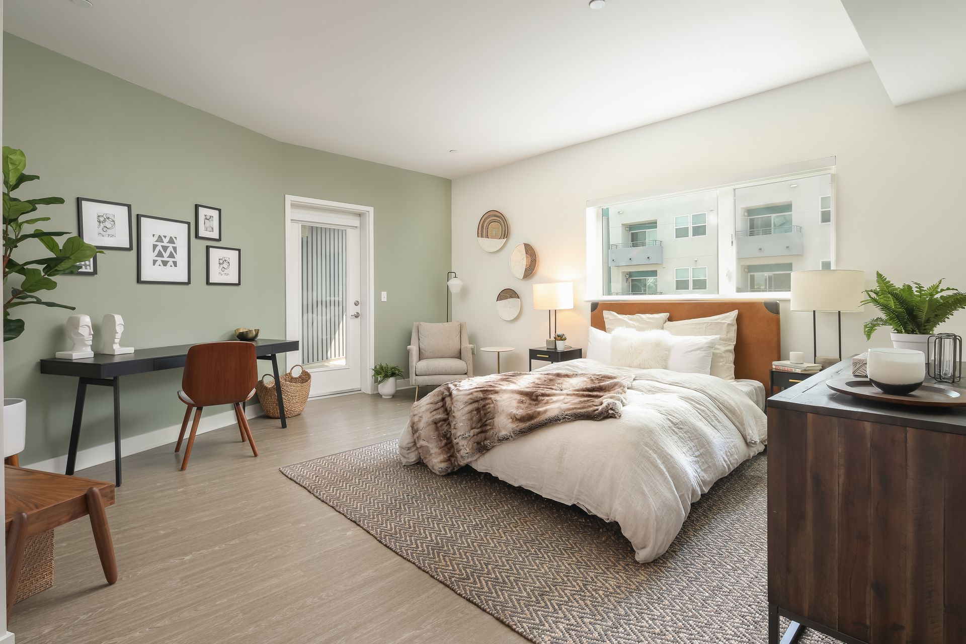 Bright bedroom with a bed, desk, woven rug, and large windows in soft neutral tones