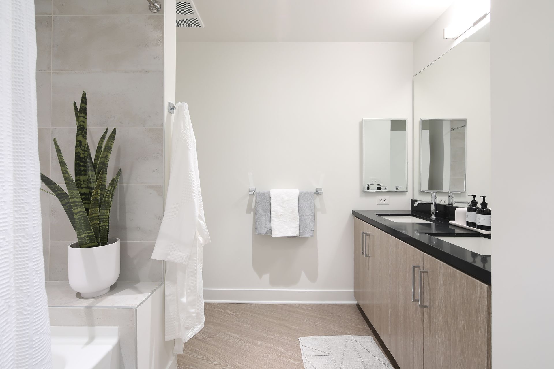 Minimalist bathroom with a potted plant, white towel rack, black vanity, and wall mirror.