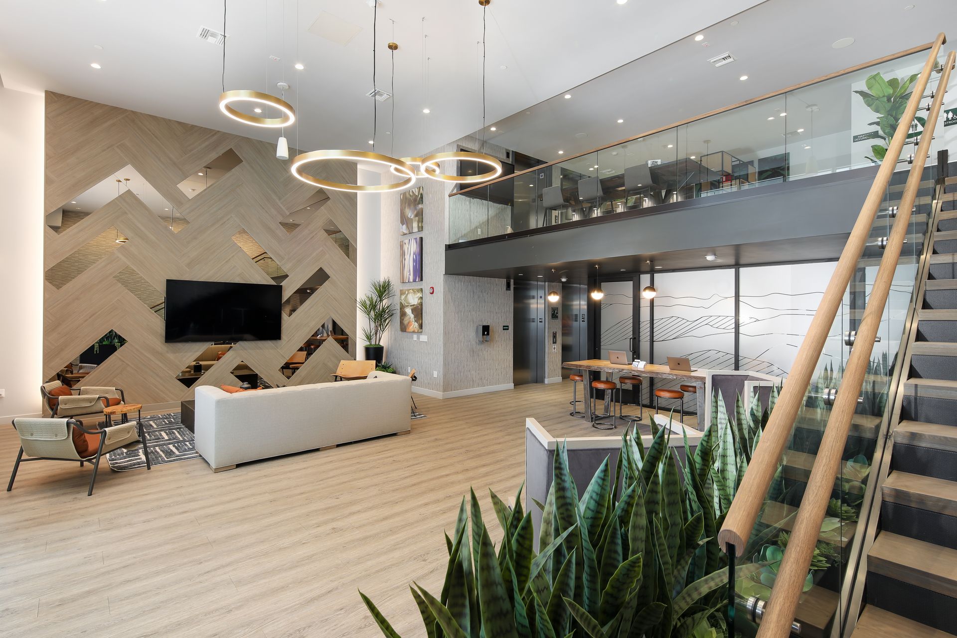 Modern apartment lobby with lounge seating, pendant lights, wood flooring, and mezzanine balcony