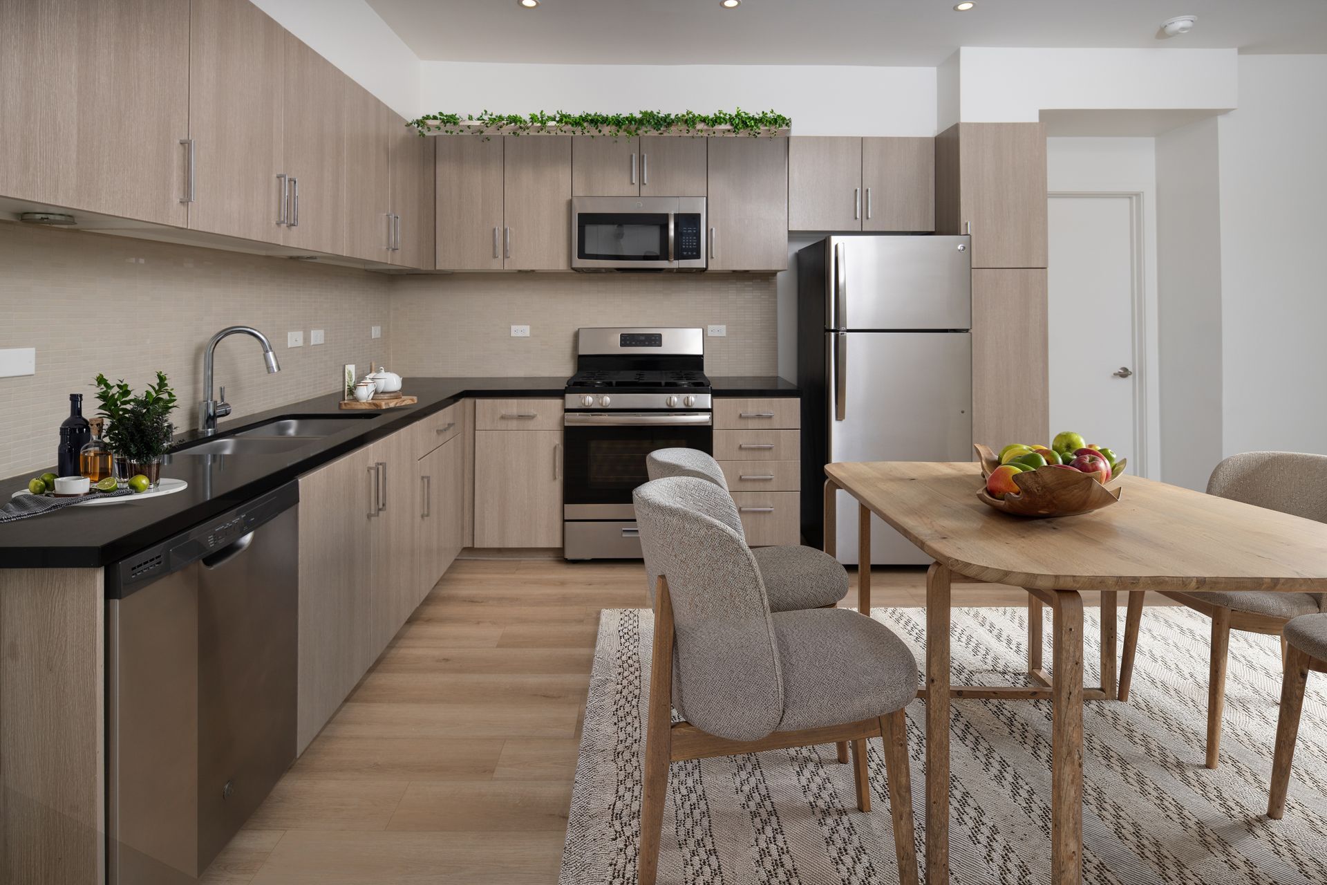Modern kitchen and dining area with wood cabinets, stainless appliances, and a table with fruit.