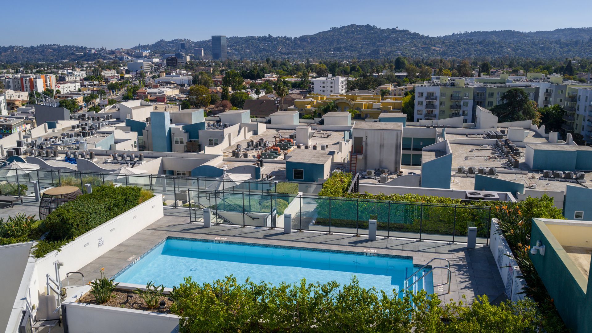 Rooftop pool overlooking a cityscape and distant hills under a clear sky