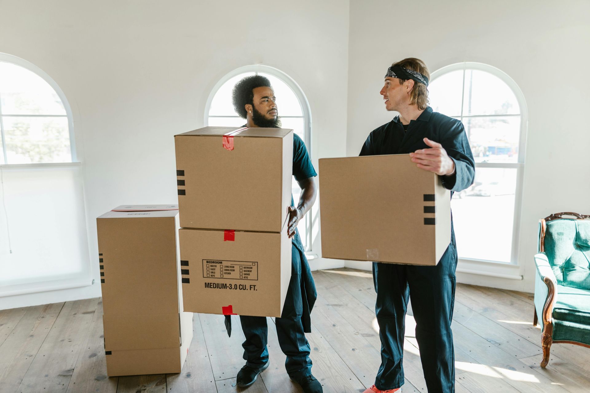 Two men are carrying cardboard boxes in a room.