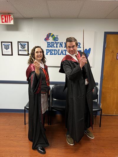 Two people in black robes pose indoors in front of a Bryn Mawr Pediatric sign.