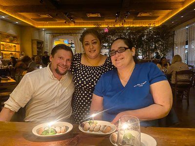 Three people smiling at a restaurant table with drinks and plates under warm lighting