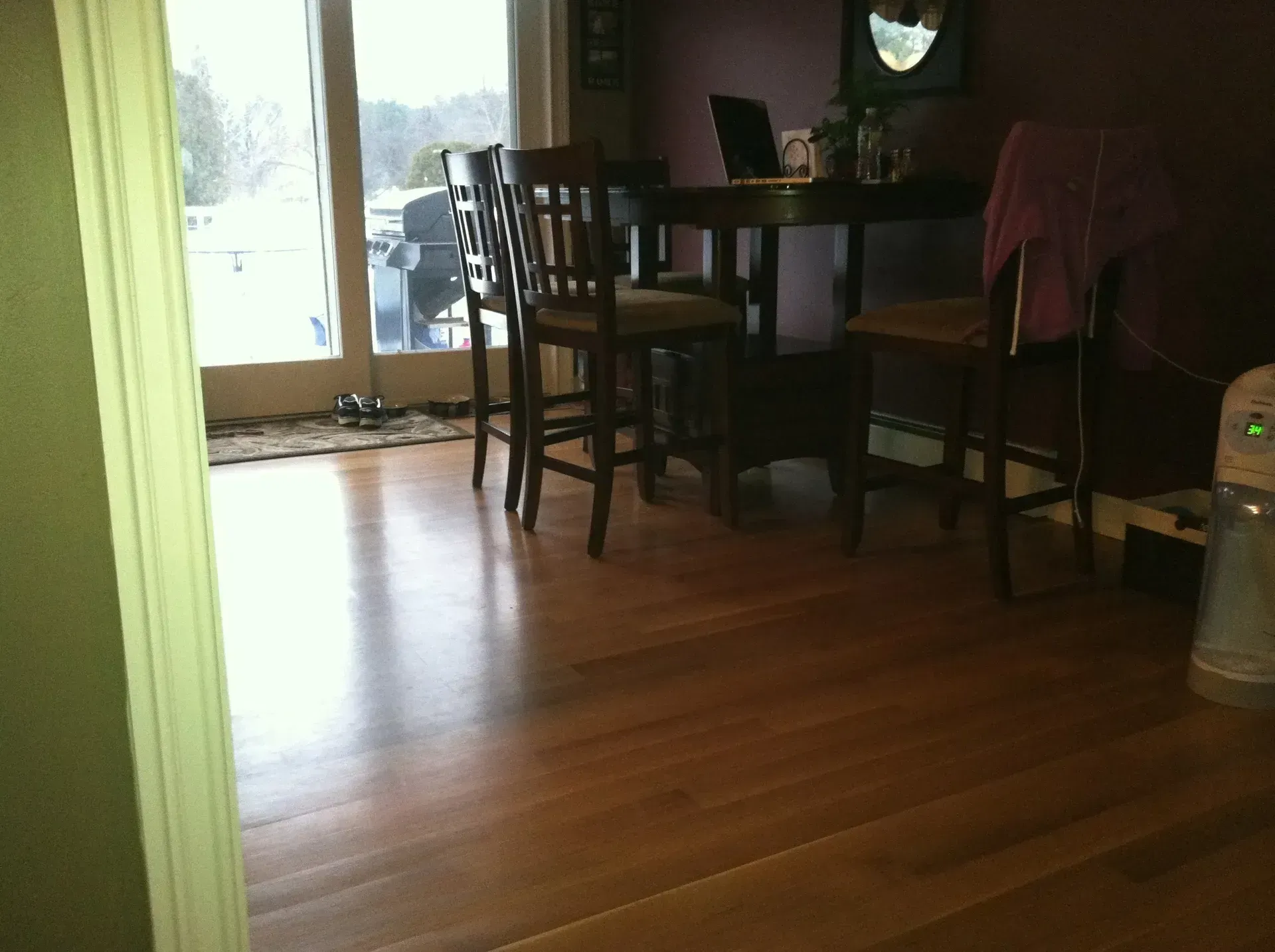 Dining area with dark table and chairs on hardwood floor near a glass door.