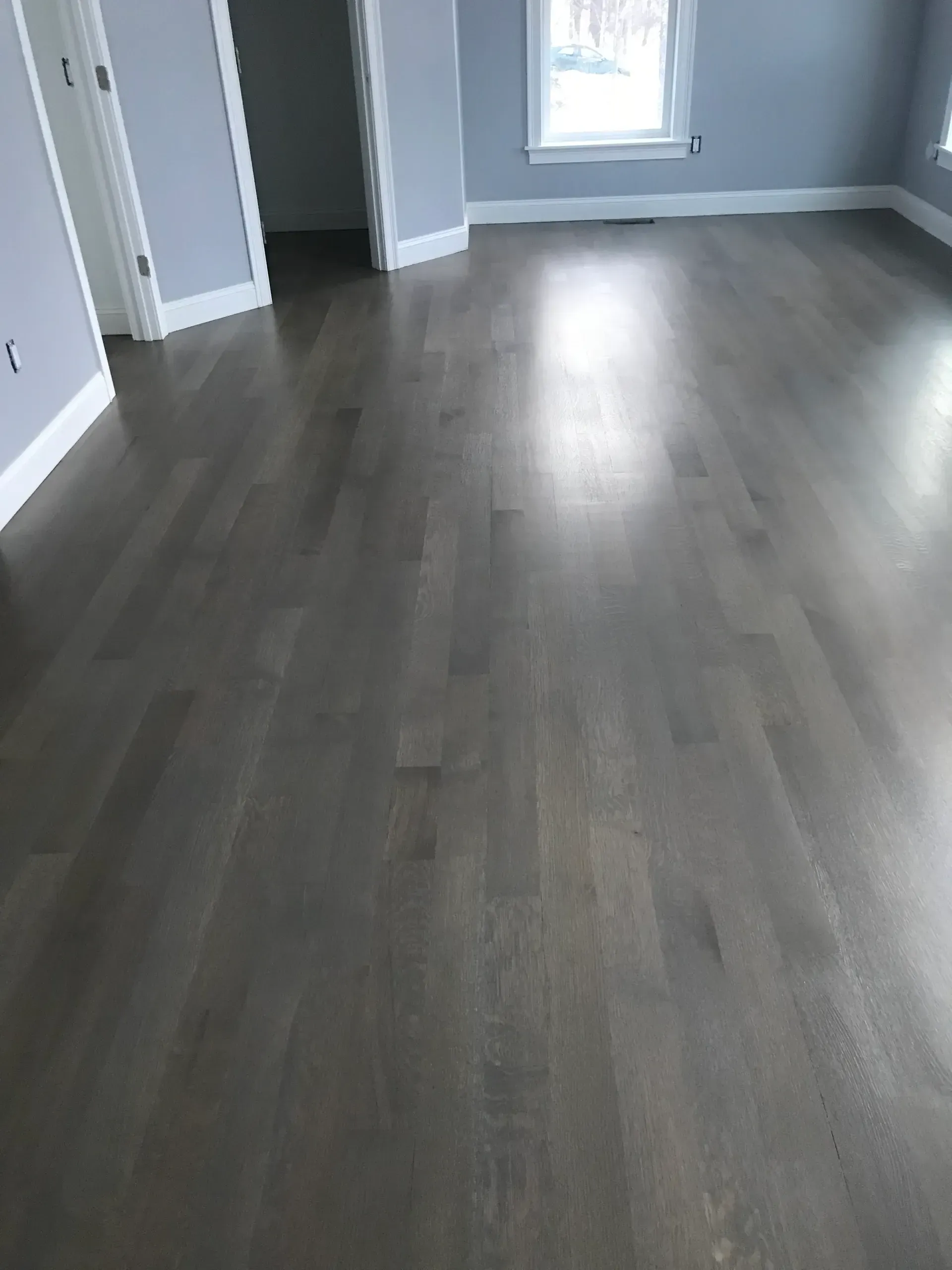 Empty room with gray wood floors, light gray walls, and a window at the far end.