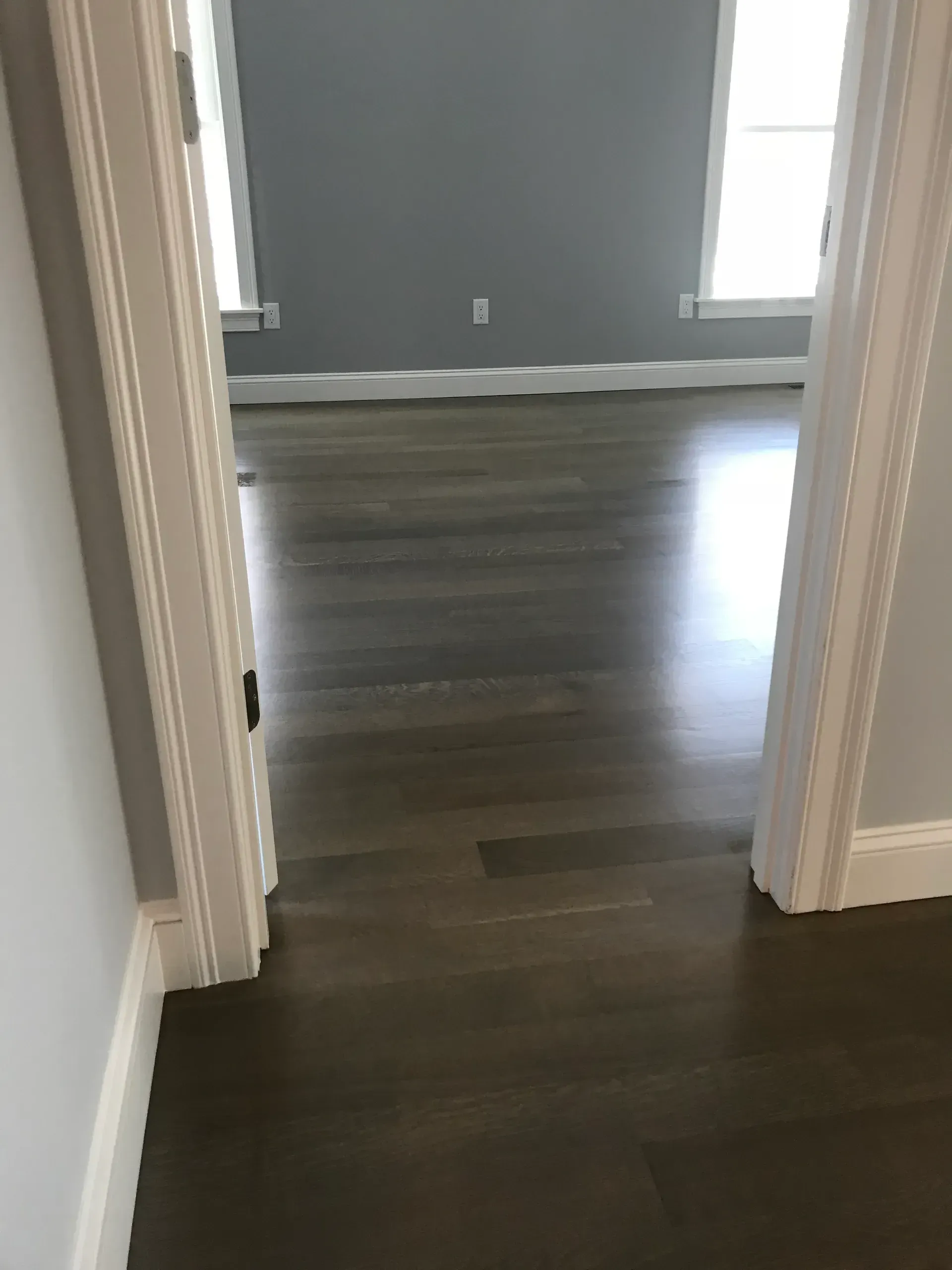 Hallway doorway leading to an empty room with dark wood floors and gray walls.