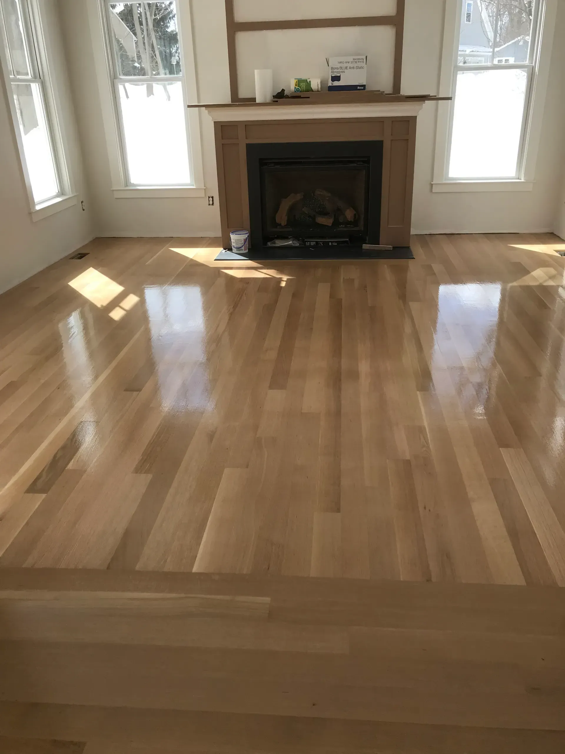Empty living room with polished hardwood floors and a fireplace centered between windows.