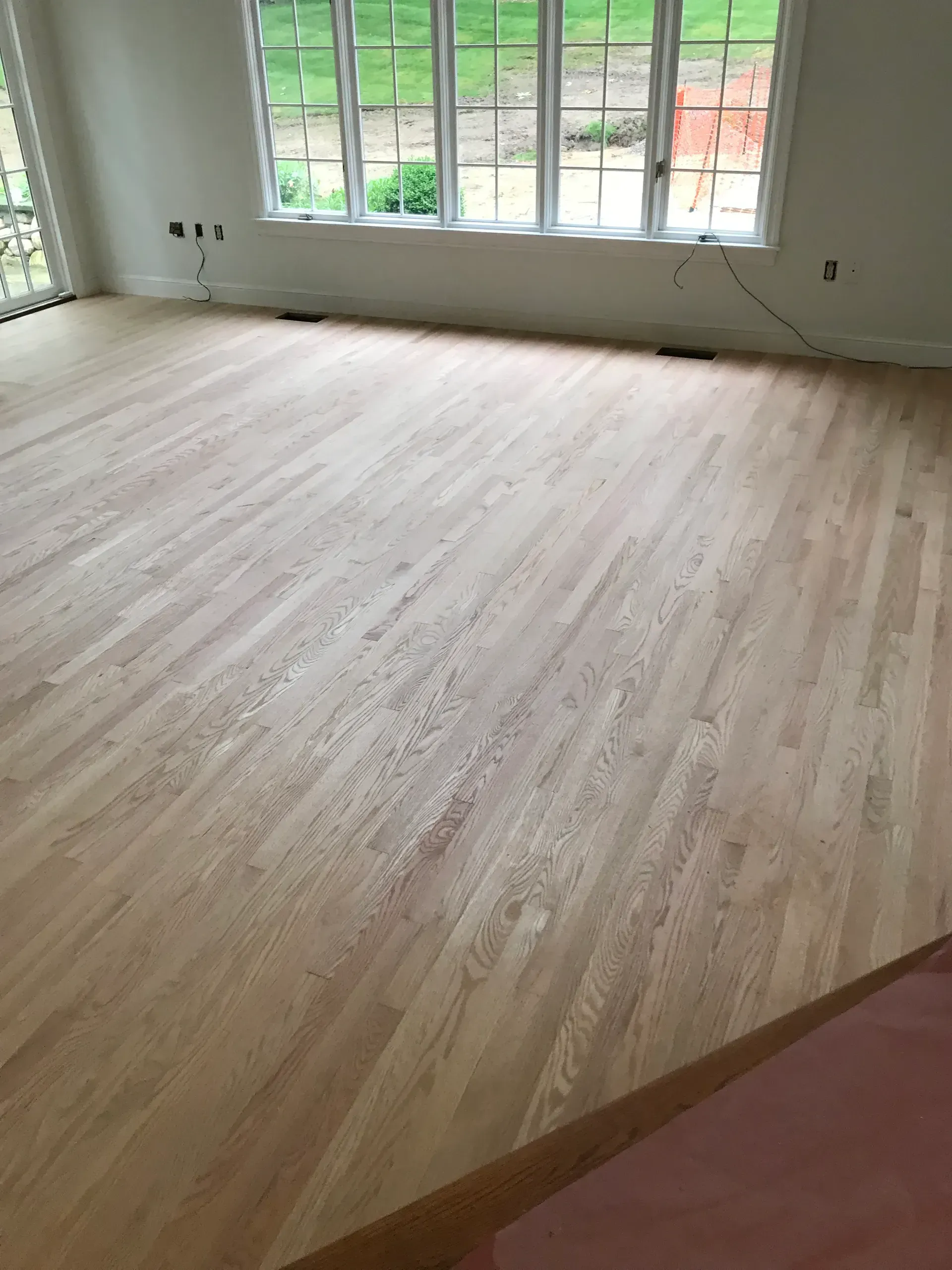 Empty room with light wood floor and large windows overlooking a green yard