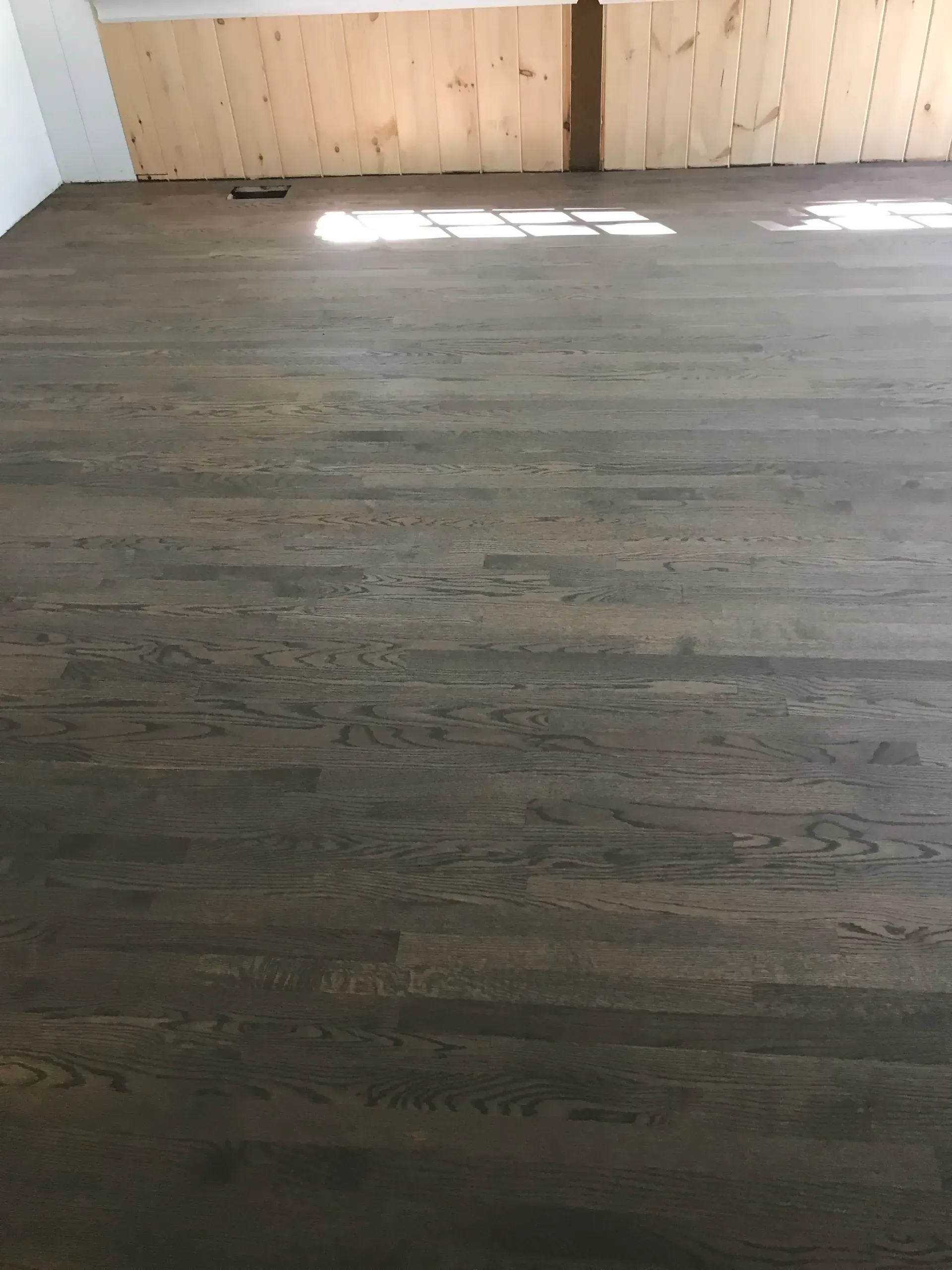 Empty room with dark wood floor and sunlight on a light wood wall panel.
