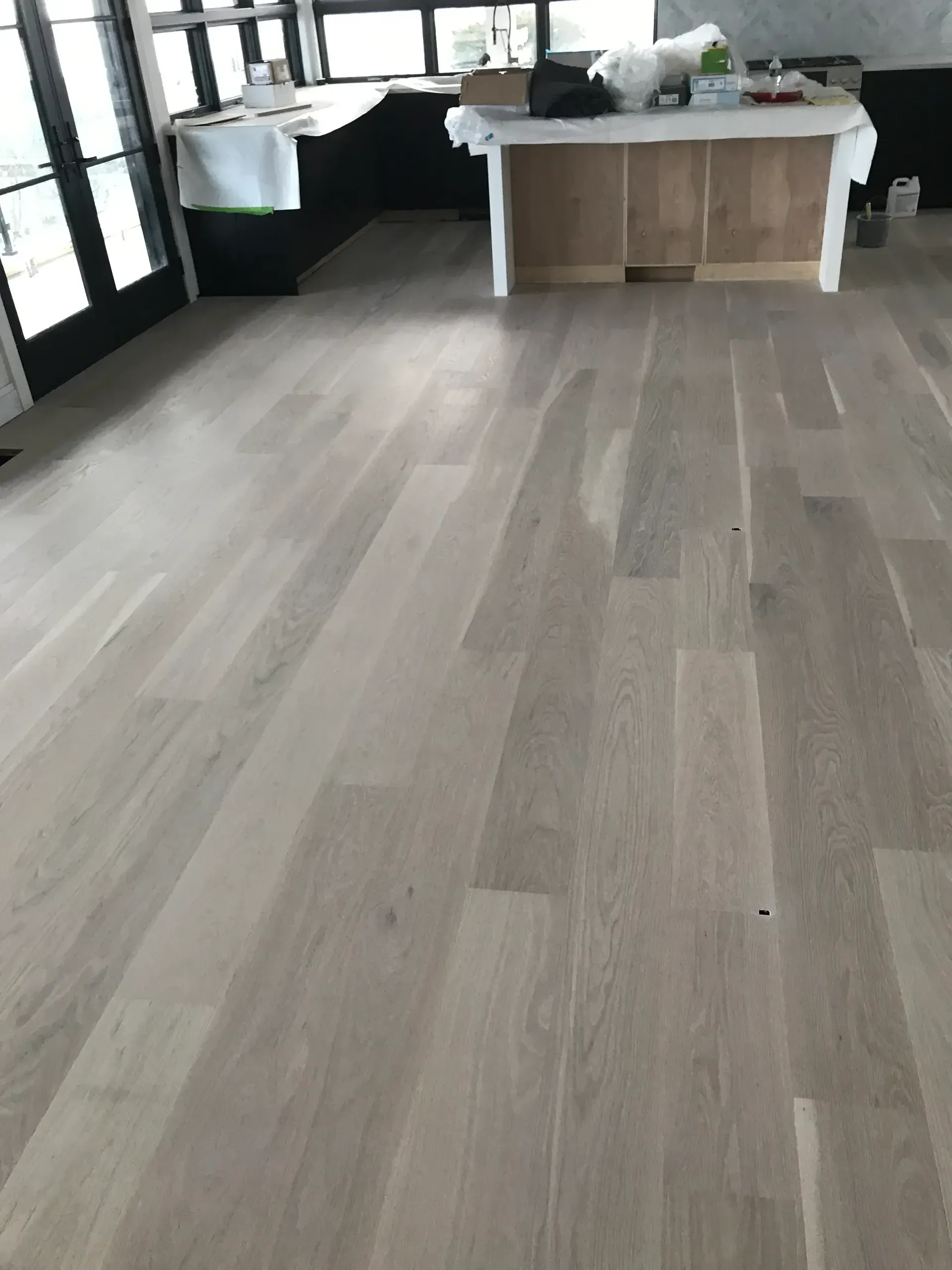 Empty room with light wood flooring, large windows, and a worktable at the back.