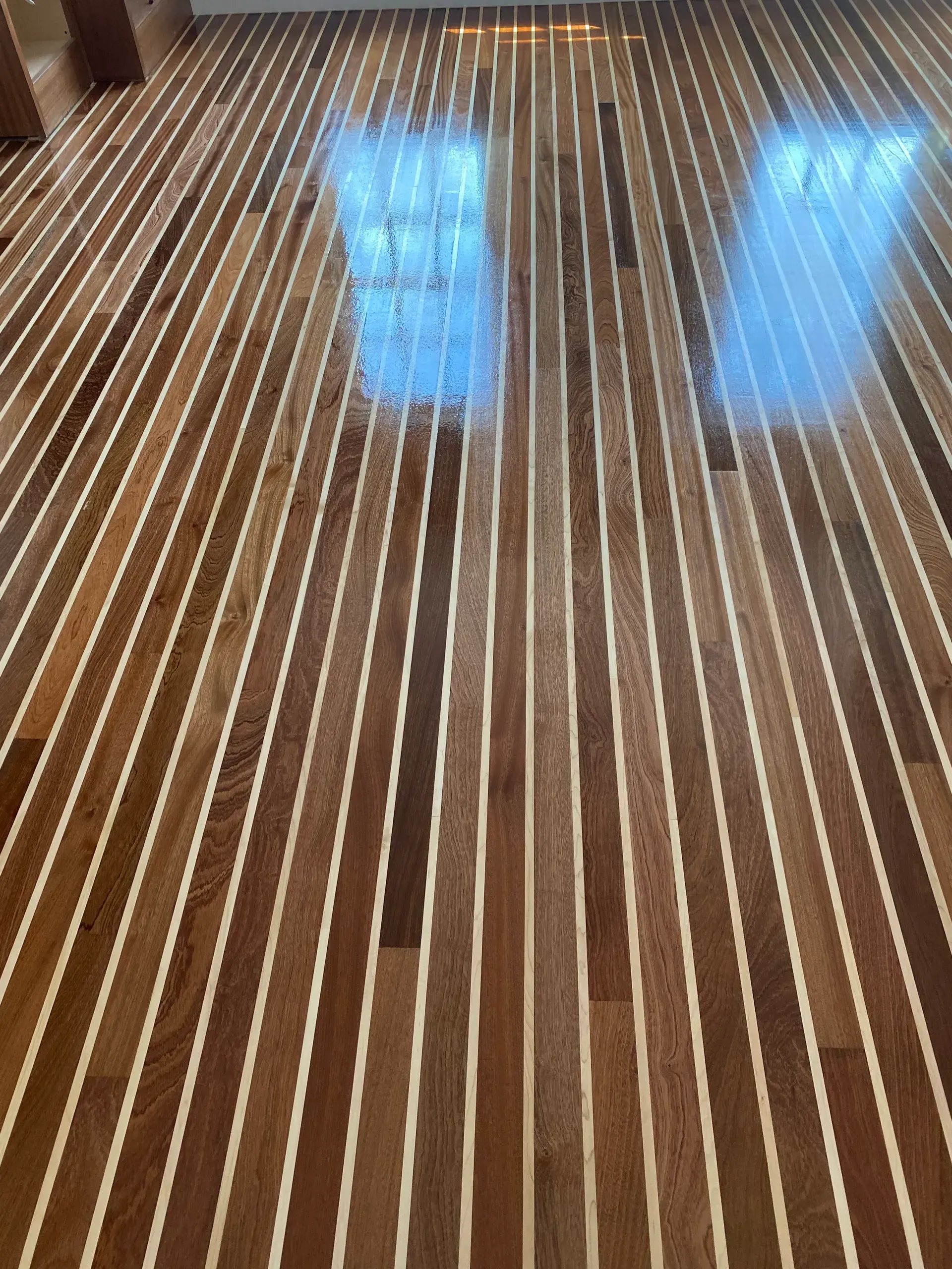 Wooden floor with bright window reflections and narrow white stripes running lengthwise