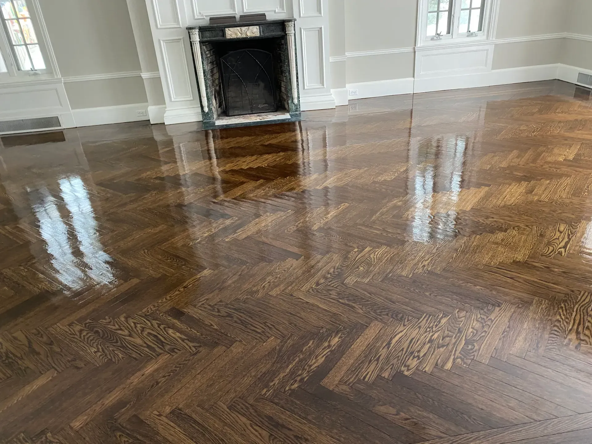 Empty polished hardwood room with a fireplace and window reflections