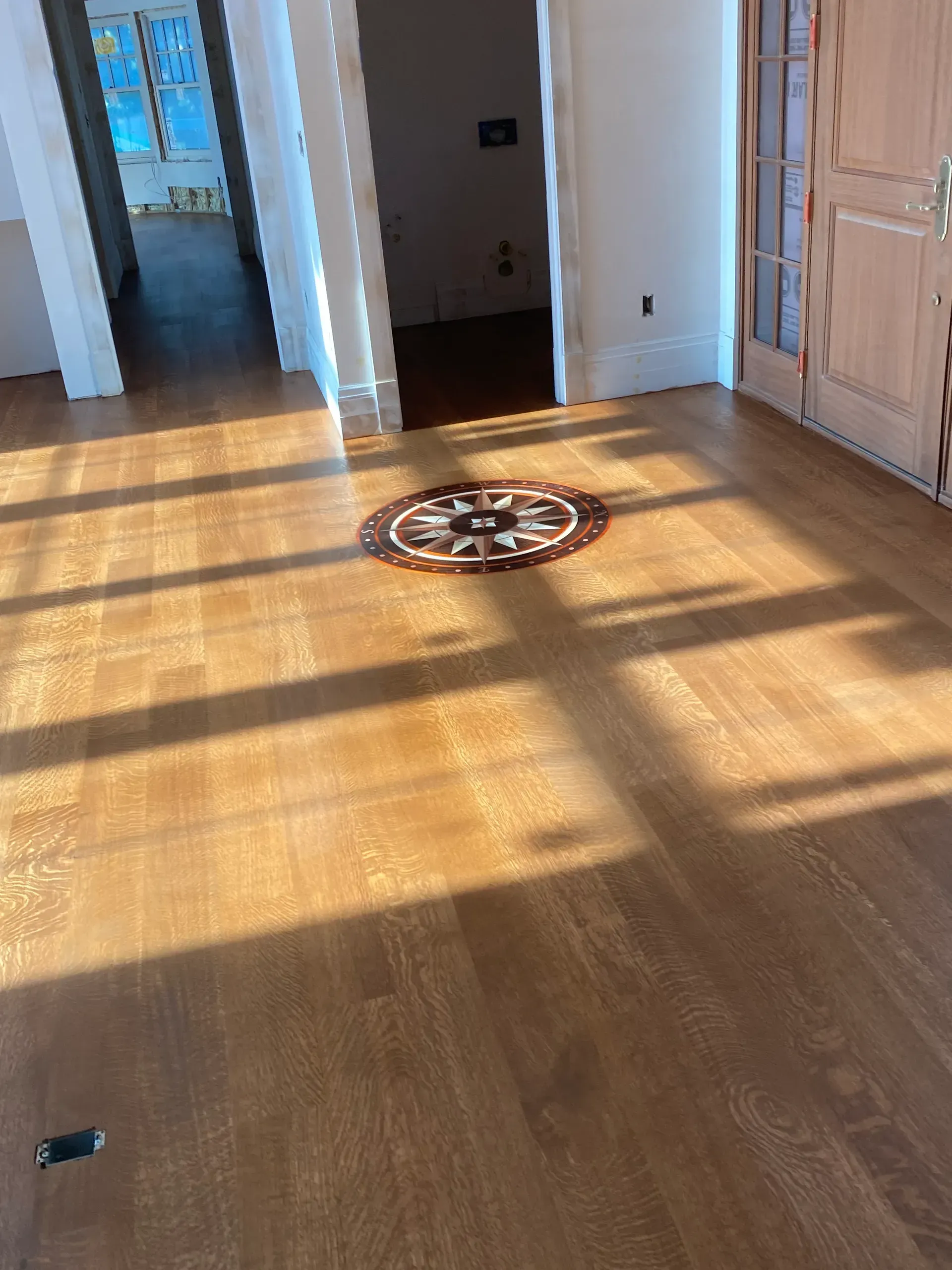 Sunlit hardwood floor in a room with white walls, doorways, and a large wooden cabinet or closet.