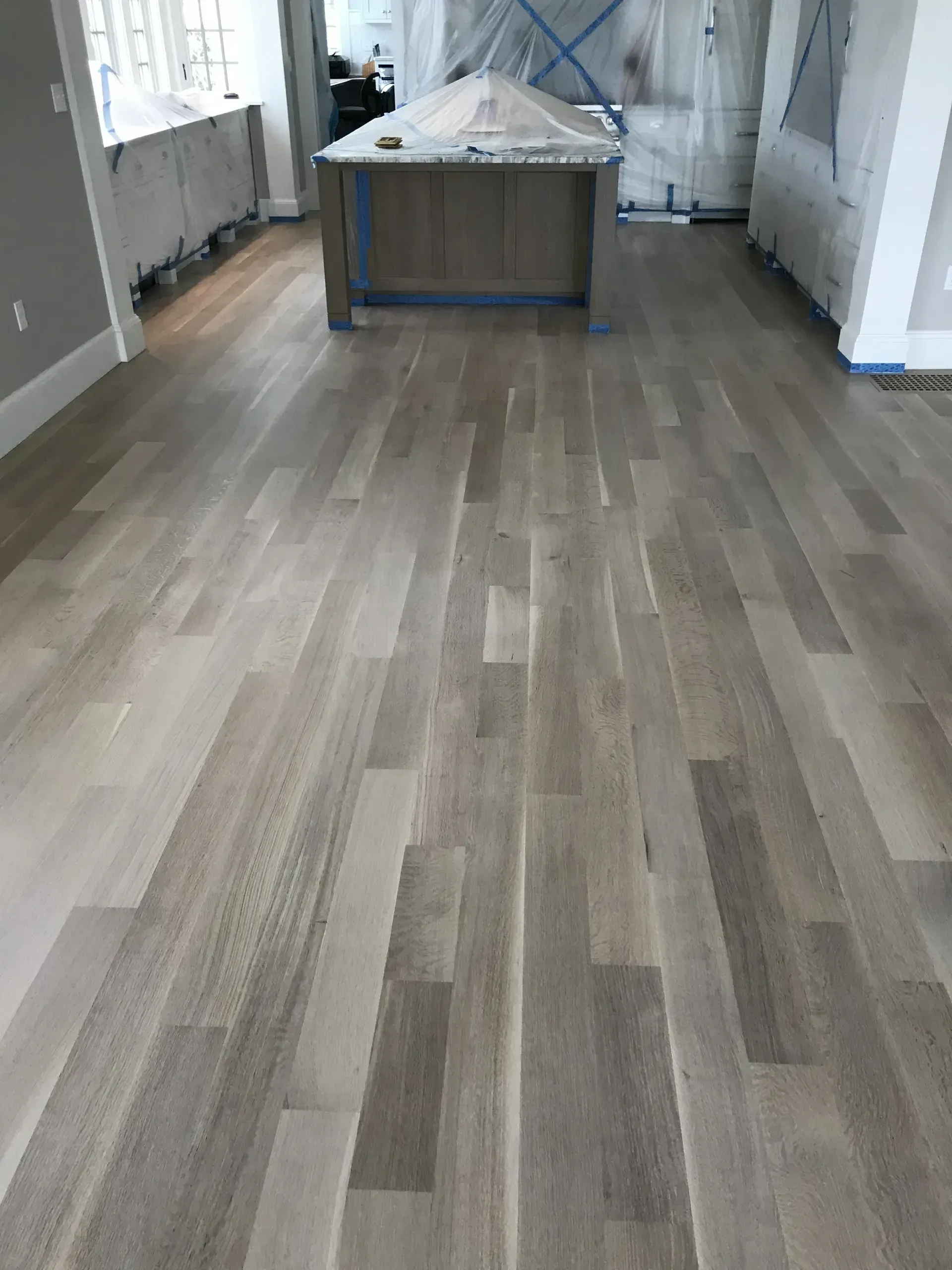 Empty room with gray wood floors and a large kitchen island in the center.