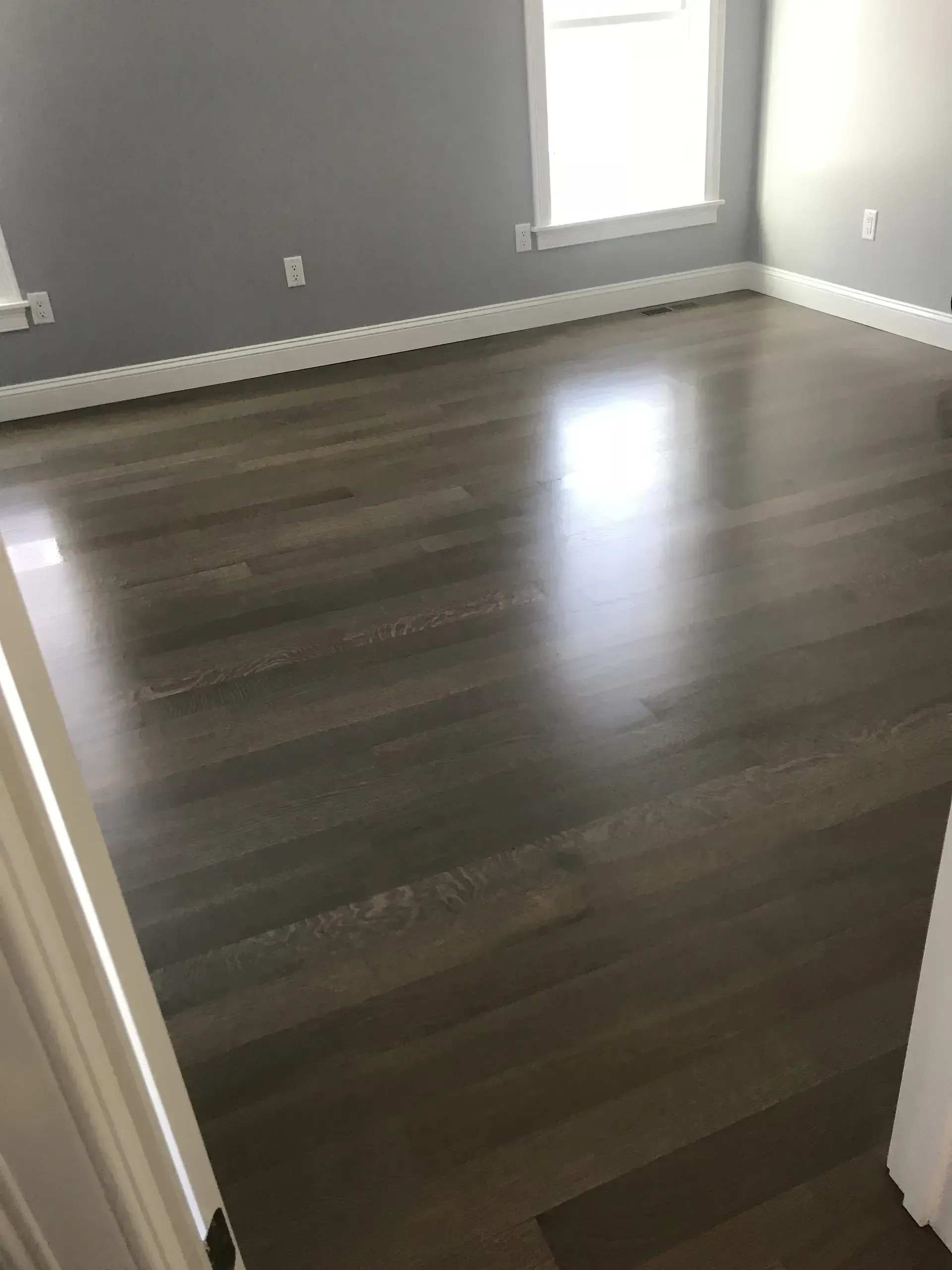 Empty room with dark wood floors, gray walls, and a window letting in daylight