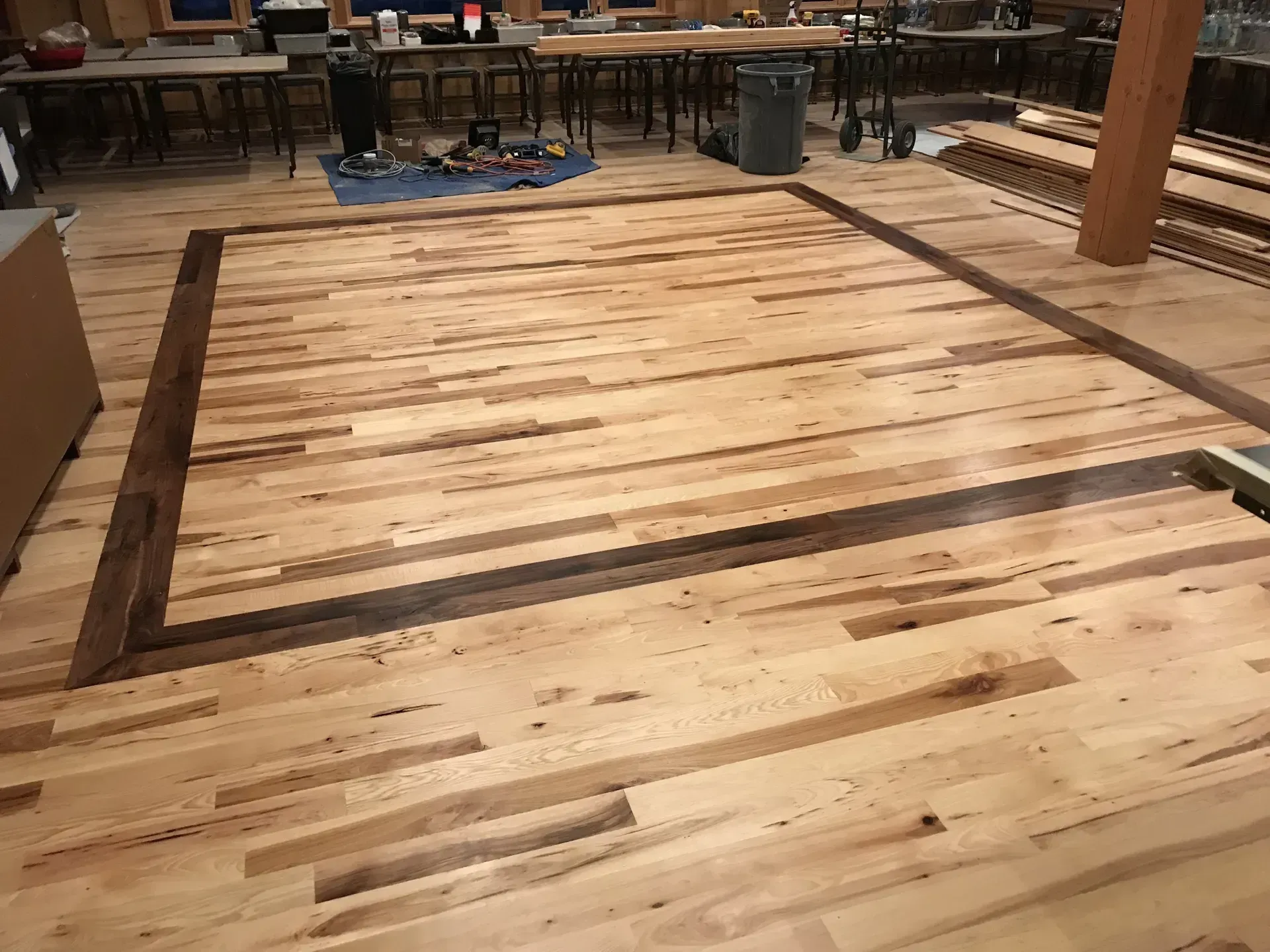 Wooden floor frame under construction in a workshop, with planks laid inside the rectangular border.