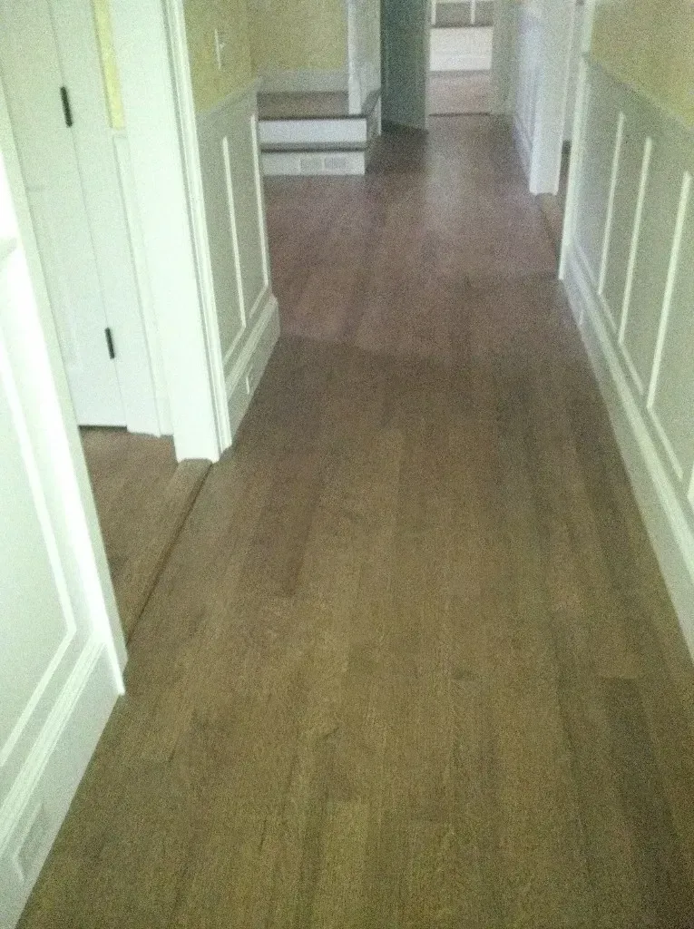 Narrow hallway with beige walls, white trim, and wood flooring leading to a doorway.
