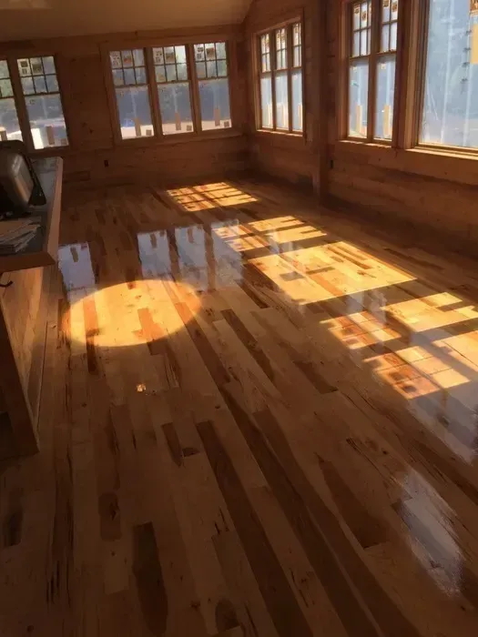 Sunlit empty room with polished wooden floors and large windows casting long shadows