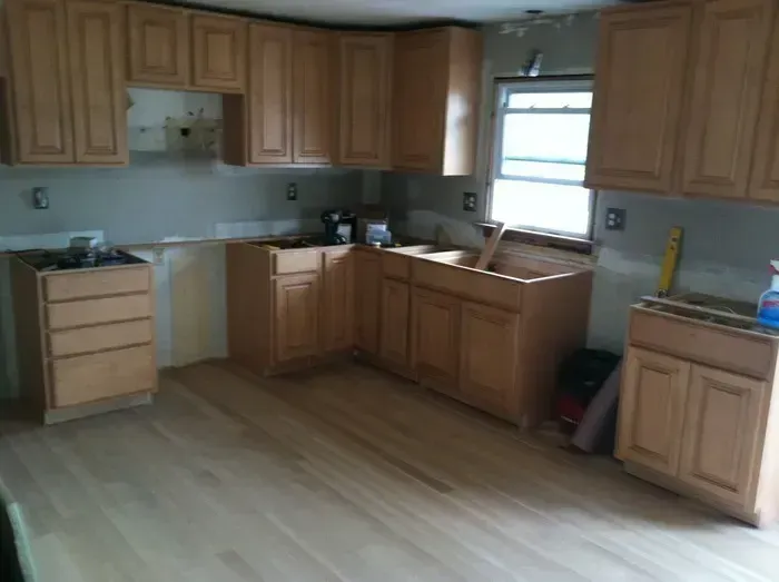 Empty kitchen with wooden cabinets, light wood floor, and a window over the sink.