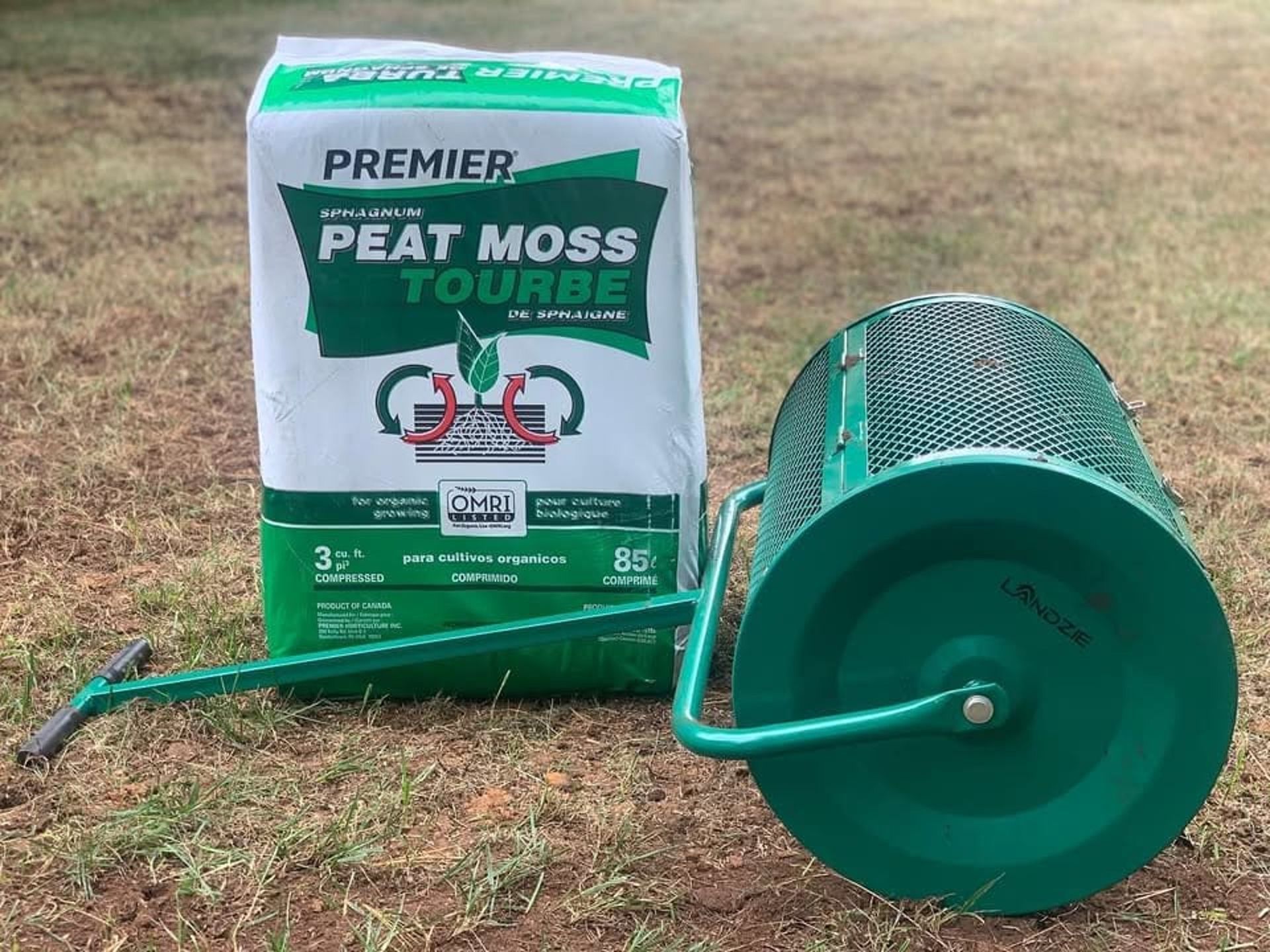 A bag of Premier Peat Moss sits on a lawn next to a green mesh lawn roller used for spreading topdressing.