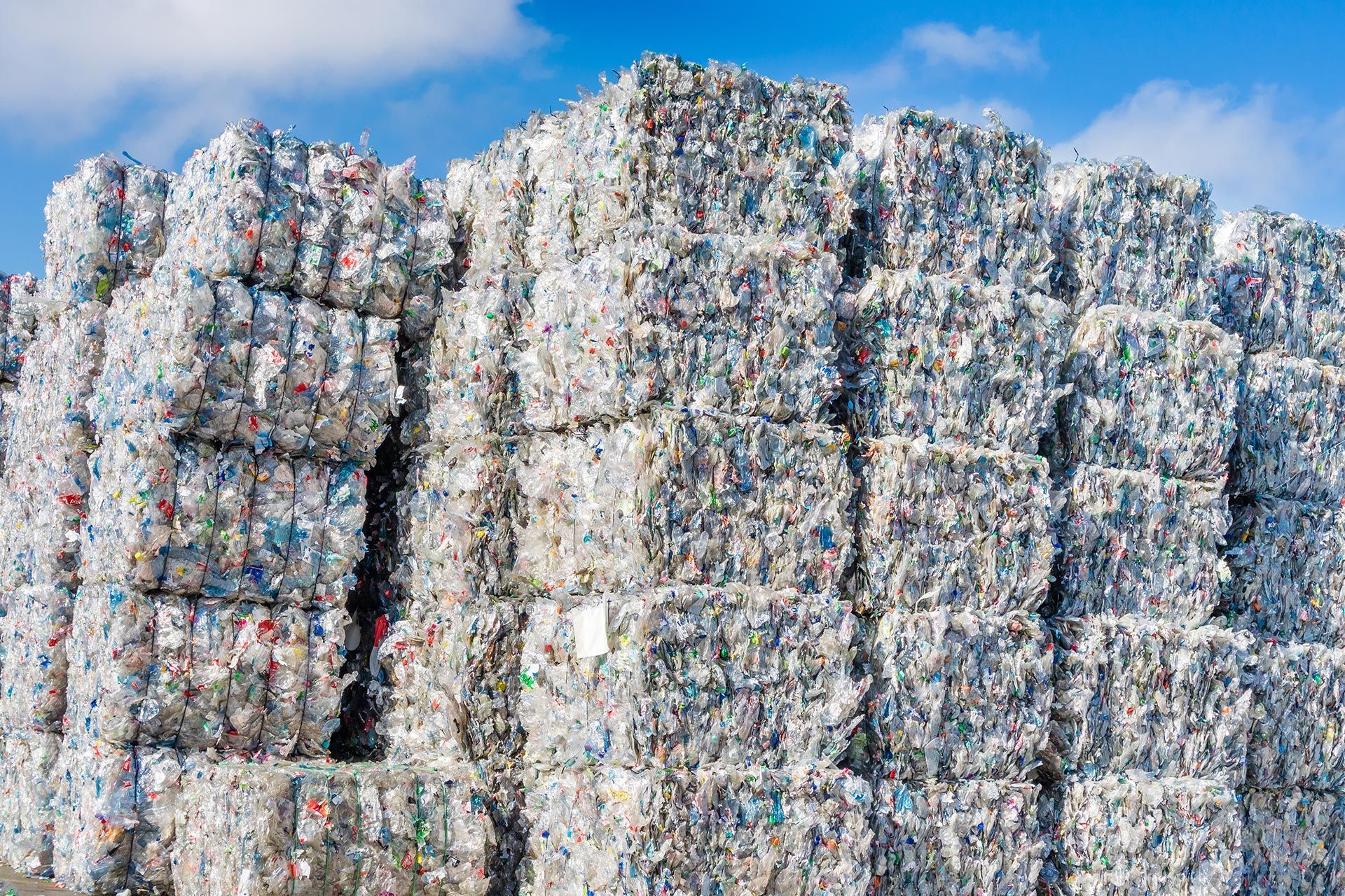 Large stacked bales of compressed plastic waste at an outdoor recycling facility. Large stacked bales of compressed plastic waste at an outdoor recycling facility.