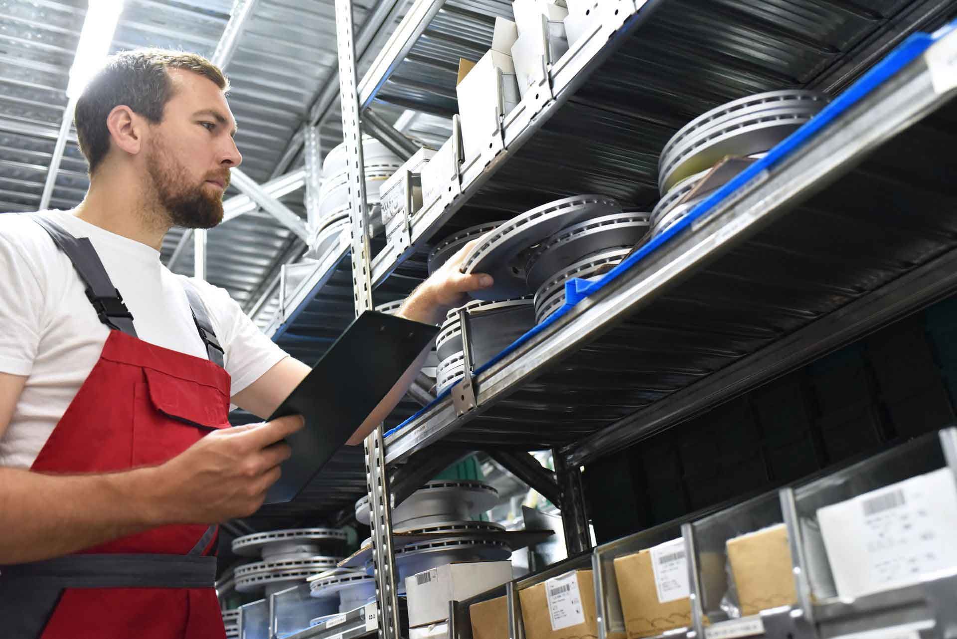 Worker in red overalls checking metal parts on storage shelves with a tablet. Worker in red overalls checking metal parts on storage shelves with a tablet.