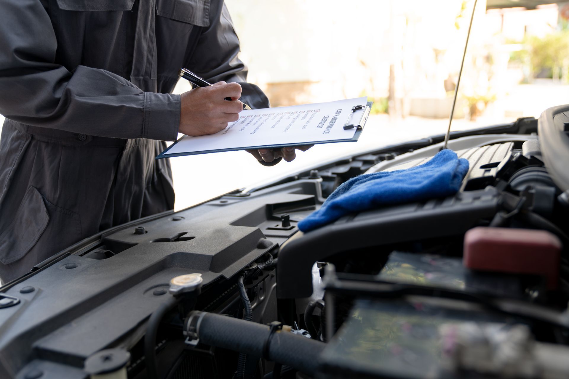 Auto technician inspecting car engine and recording maintenance details during vehicle service.