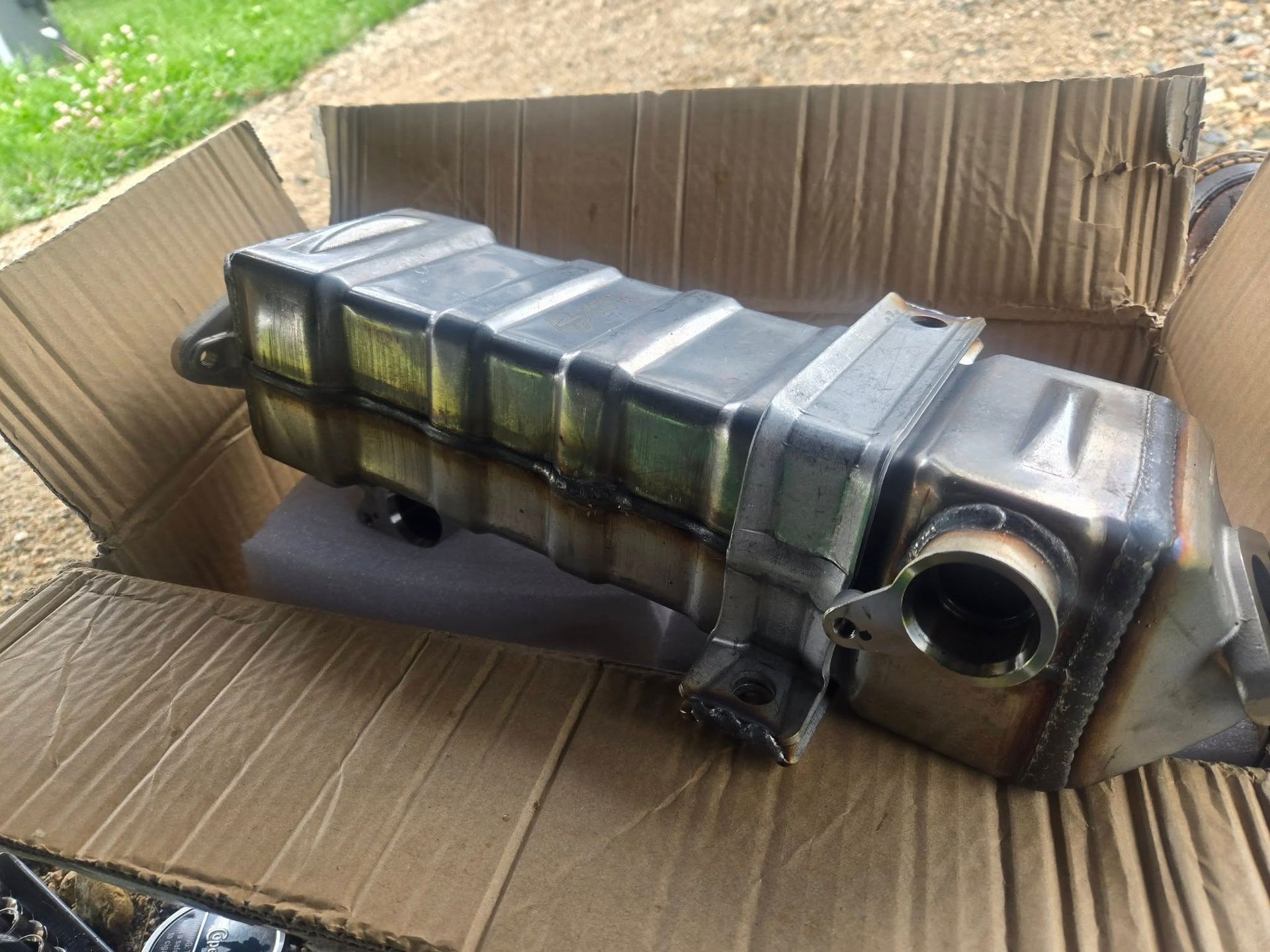 A metallic rectangular automotive part, likely an intercooler, sits inside a brown cardboard box.