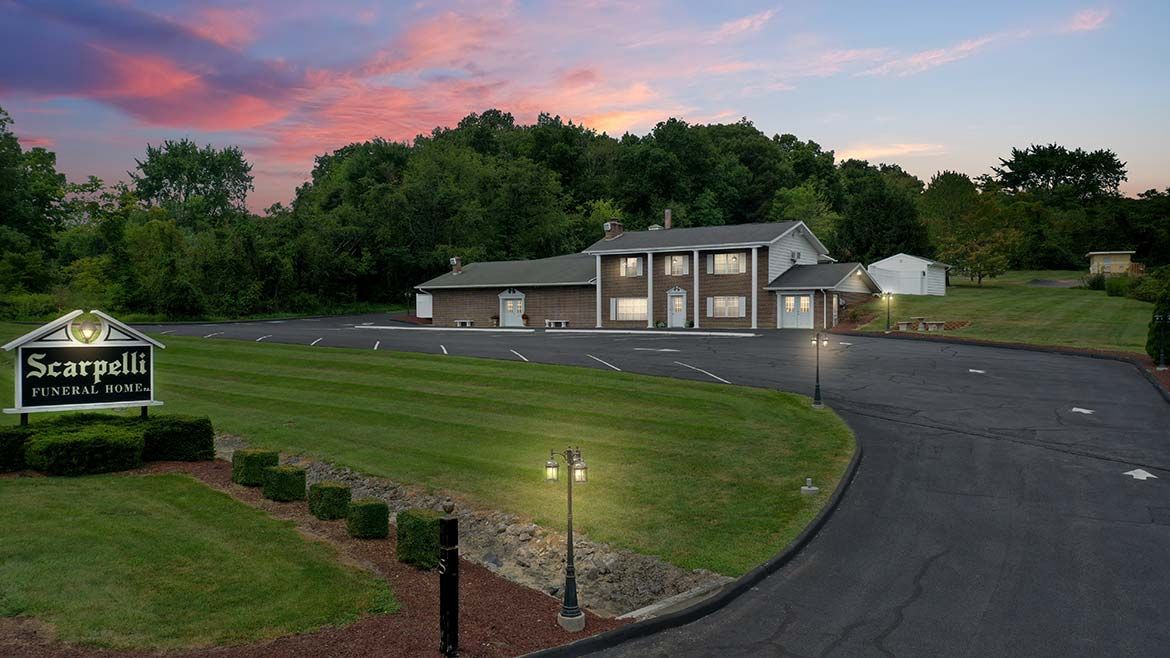 Suburban office building at dusk with lit entrance, curving driveway, and landscaped lawn under pink sky