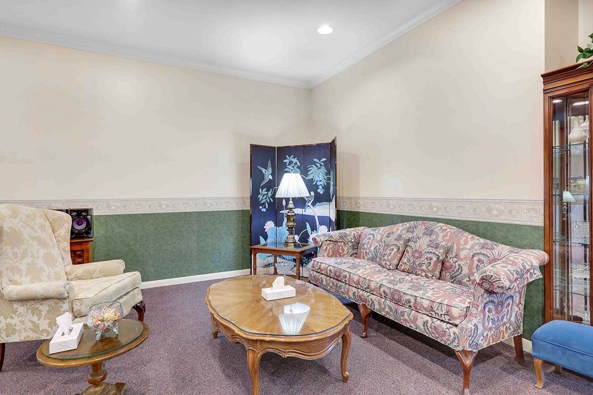 Cozy living room with floral sofa, glass coffee table, armchair, and window with curtains