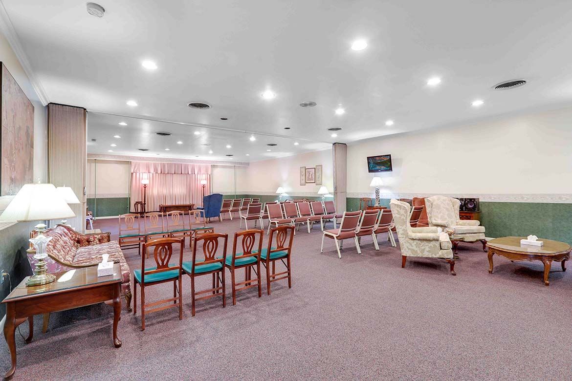 Bright lounge with bar seating, sofas, chairs, and recessed ceiling lights on carpeted flooring.