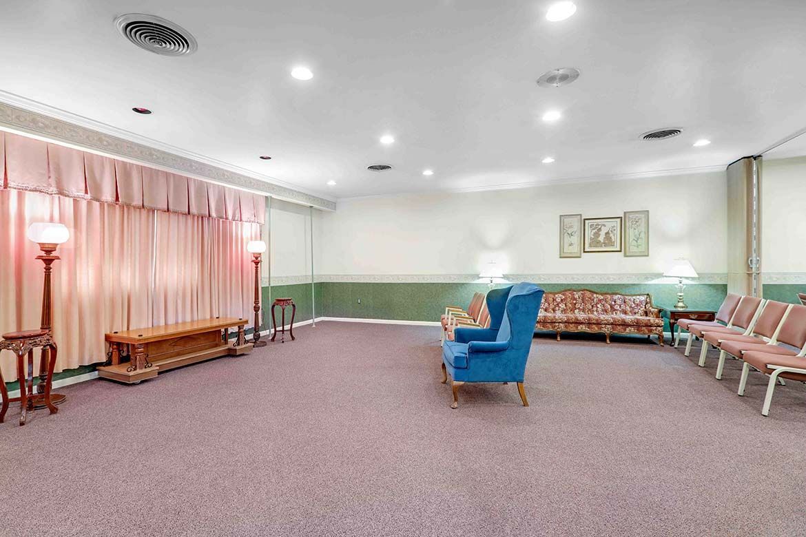 Empty carpeted waiting room with pink curtains, blue chair, and rows of beige seating