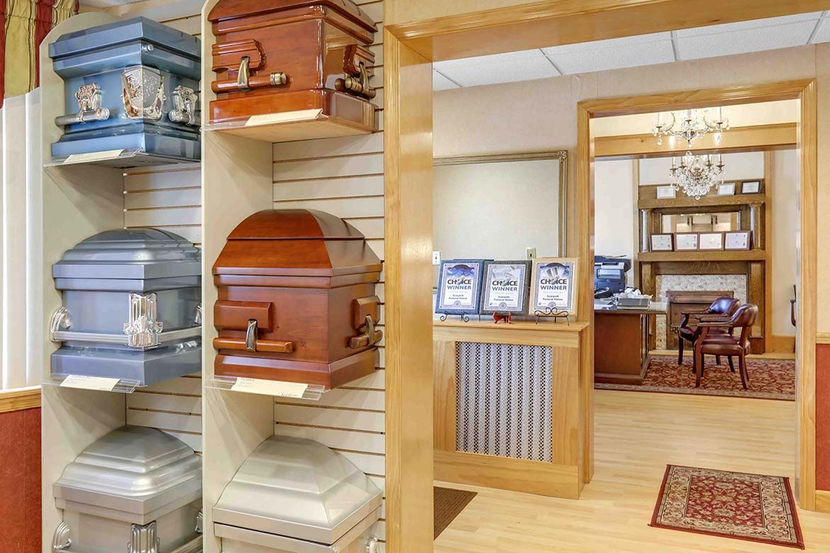 Display of colorful decorative urns and caskets in a showroom with a wooden interior and doorway to another room