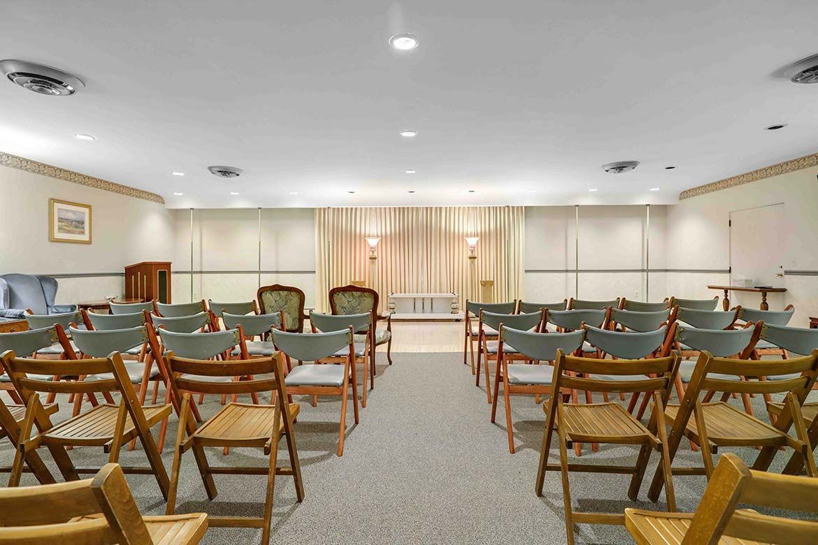 Empty banquet hall with rows of wooden chairs facing a curtained stage under bright ceiling lights