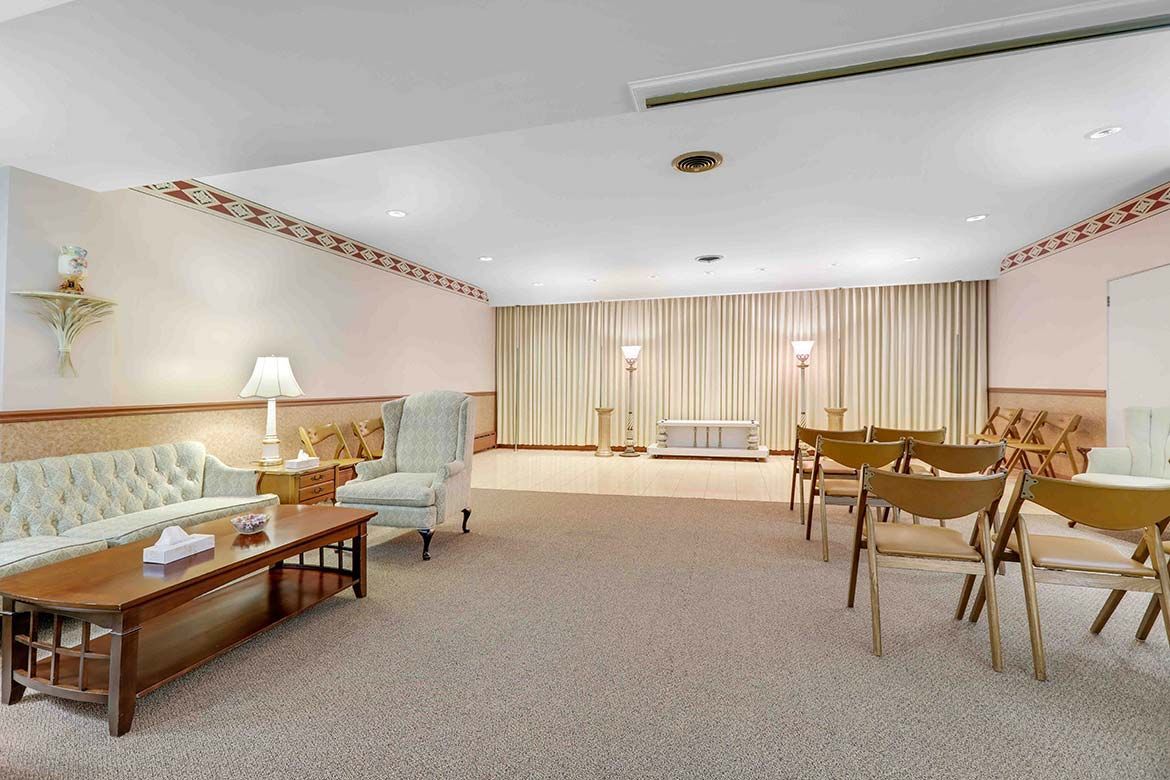 Spacious beige lounge with sofas, armchairs, tables, and curtains across the back wall