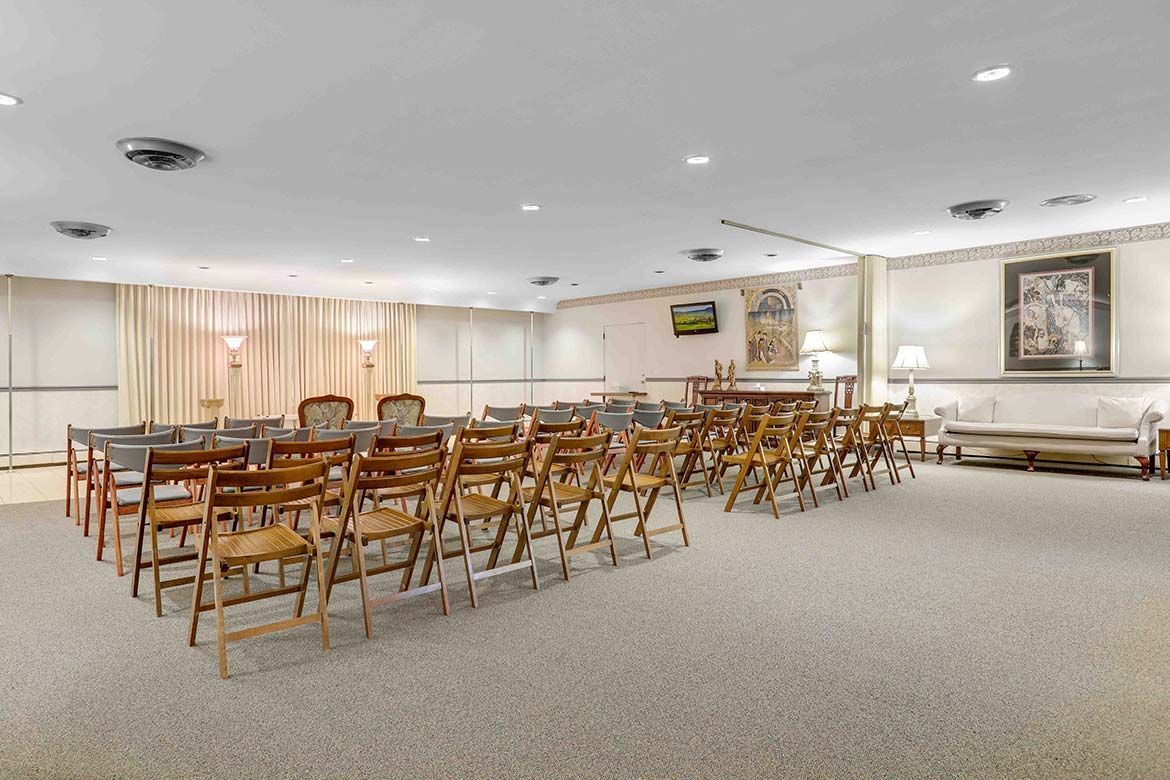 Empty church fellowship hall with rows of wooden chairs, beige carpet, and a small stage with curtains